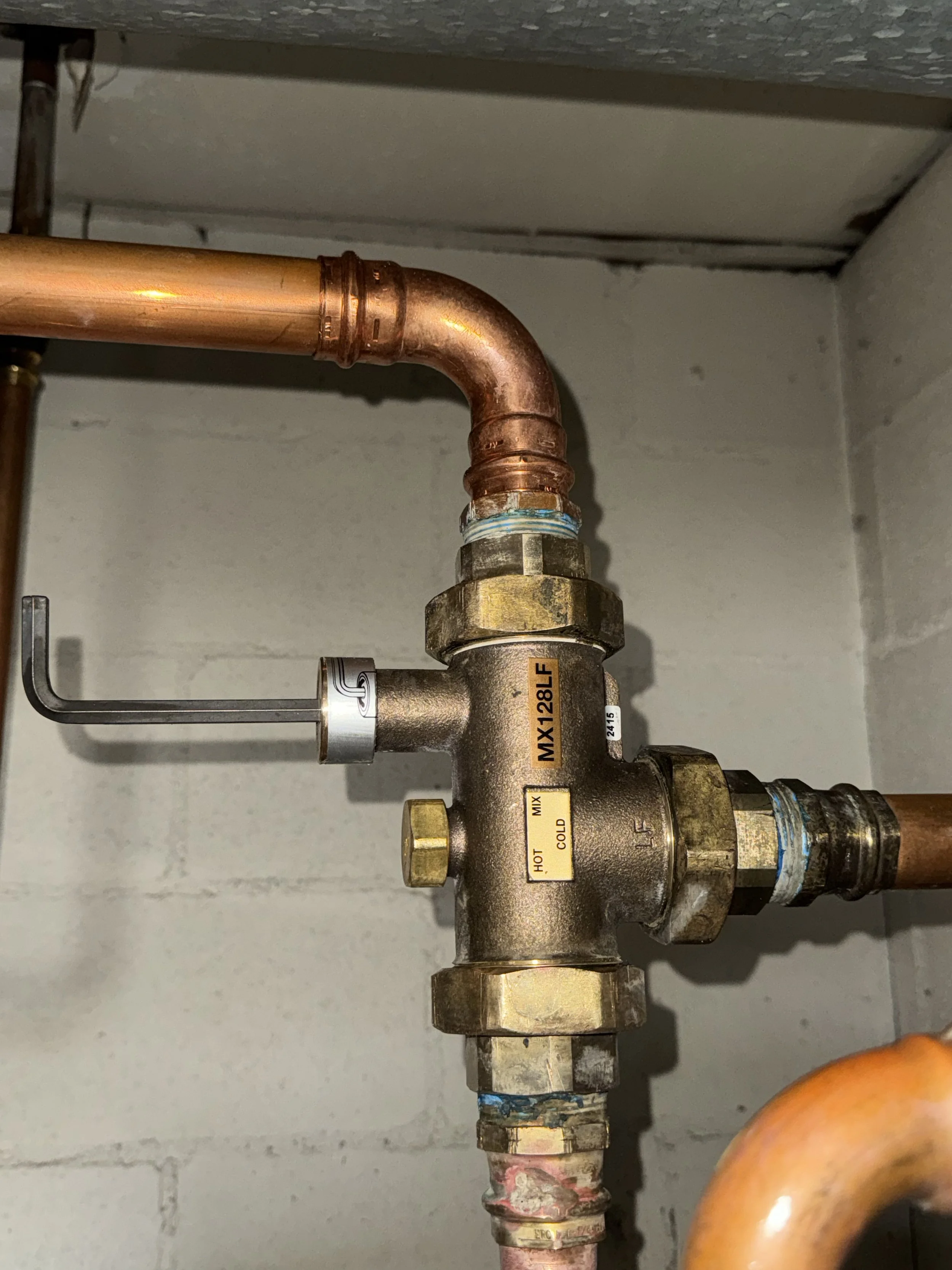 Plumbing system with copper pipes connected to a brass manifold labeled 'HOT,' 'COLD,' and 'MIX,' installed on a concrete wall.