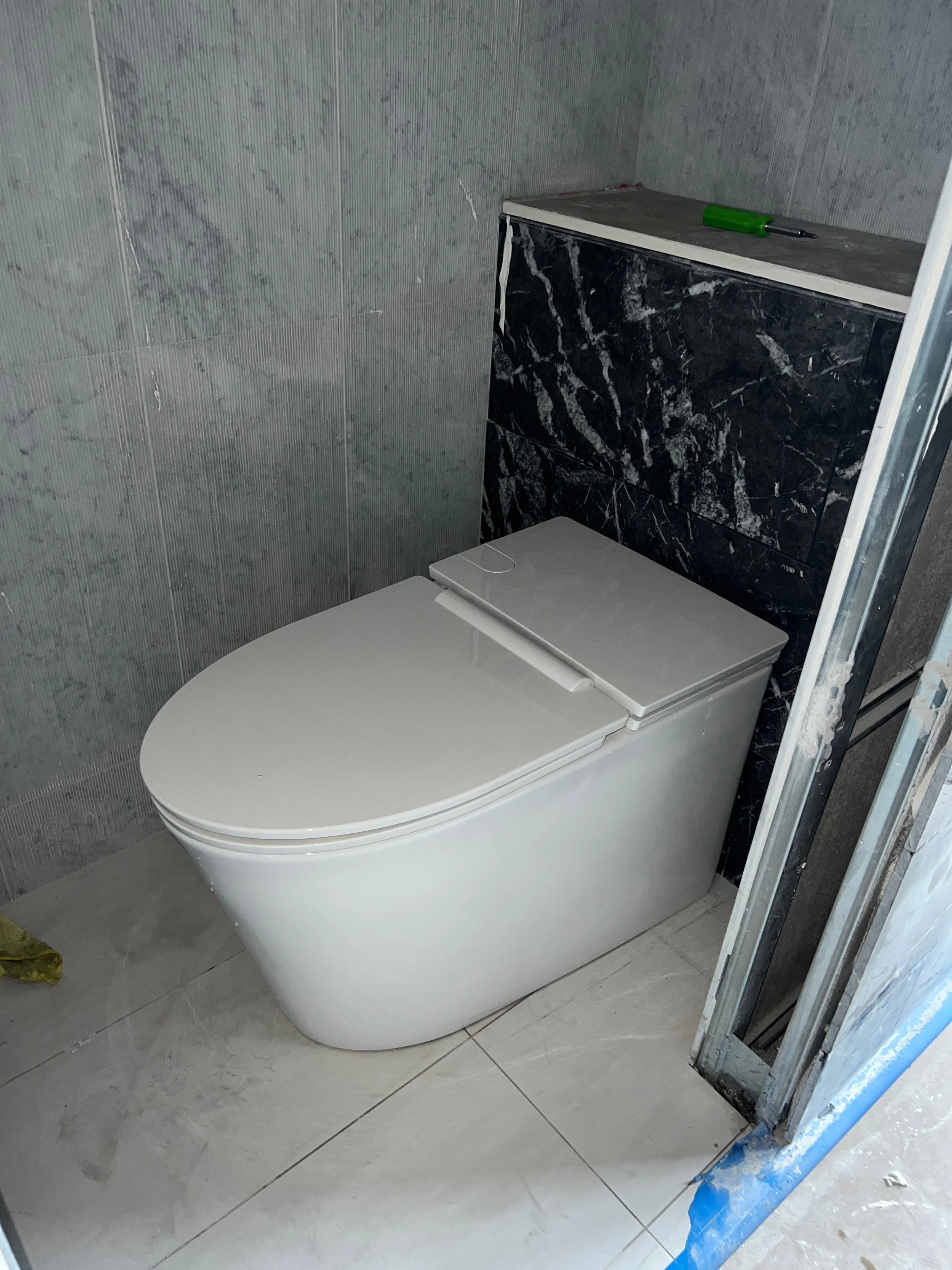 White modern toilet with a black marble tank and gray wall tiles in a bathroom under construction.