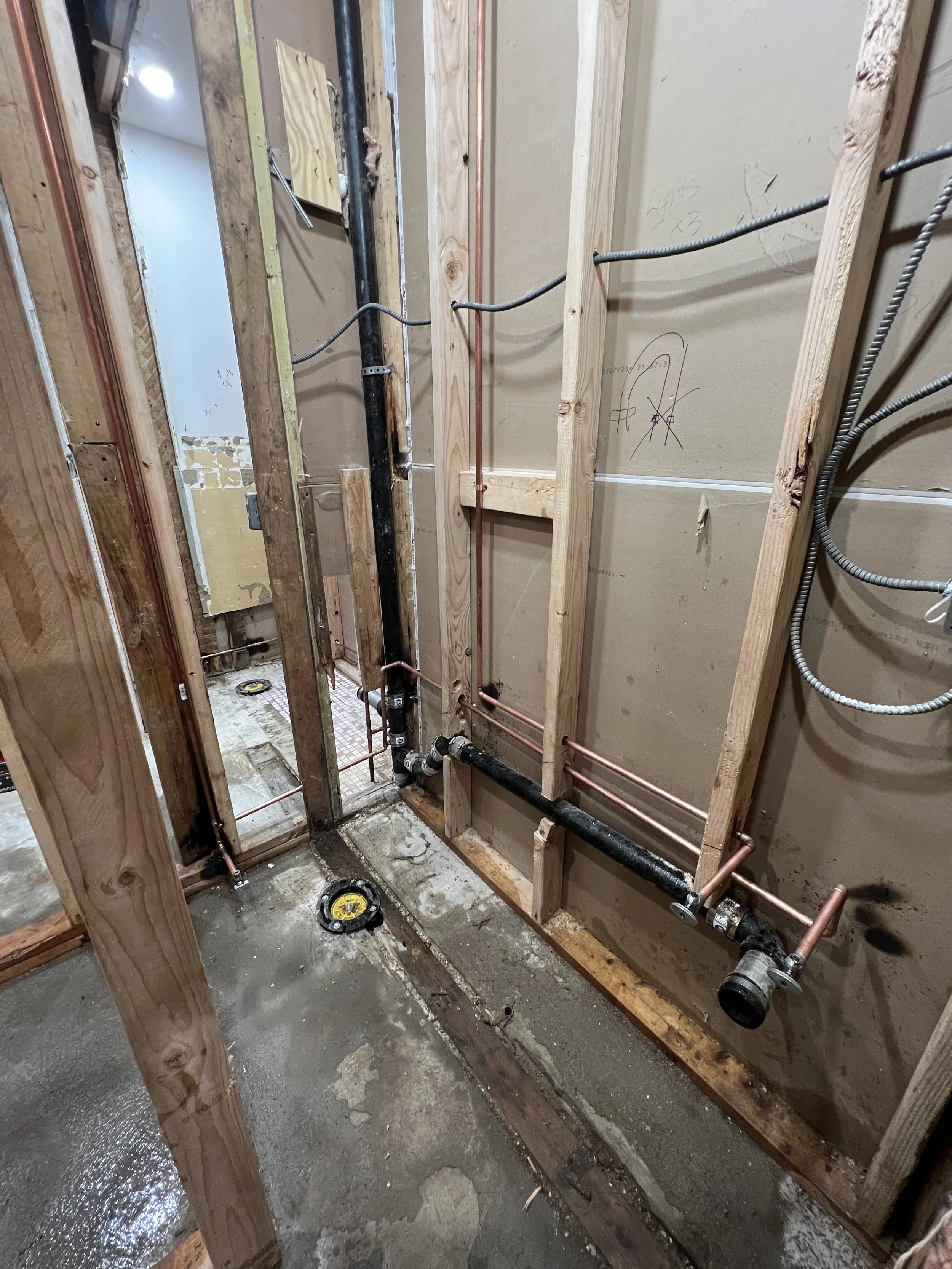 Construction site showing plumbing work with copper pipes and black pipes in a partially built room.