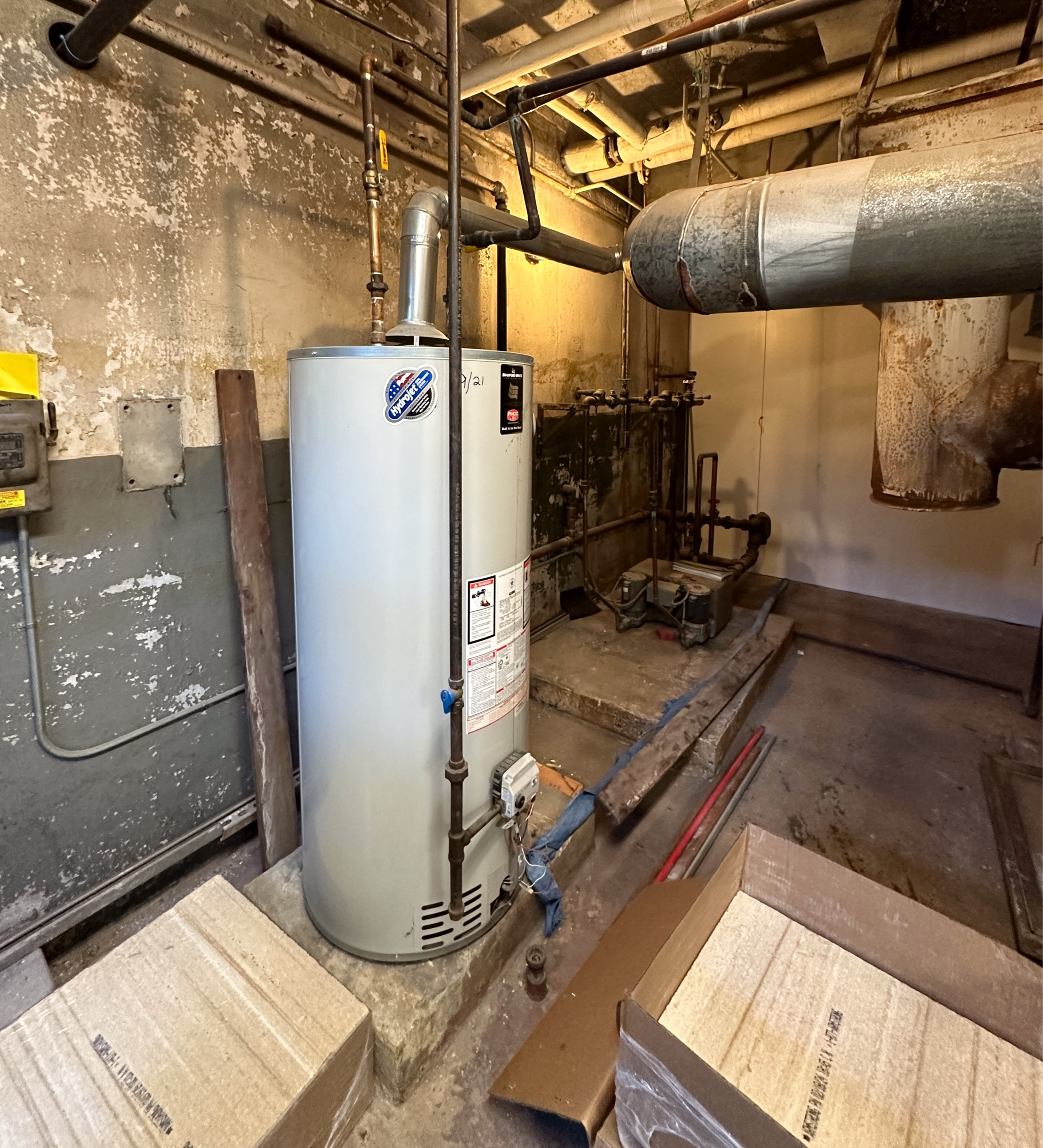 Basement utility room with a water heater, pipes, and cardboard boxes on the floor.