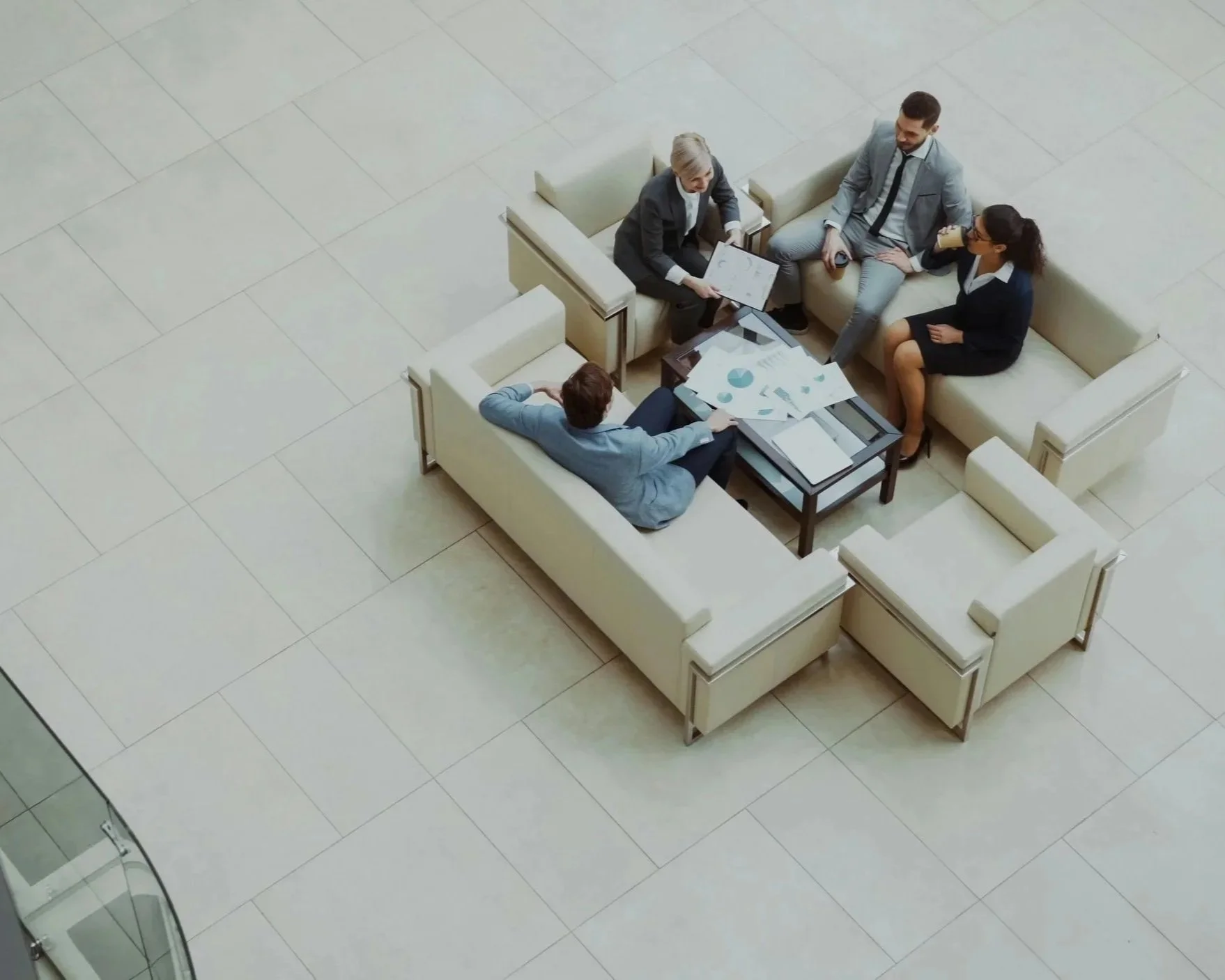 Four people sitting around a coffee table in a lobby, engaged in a business meeting with documents and charts.