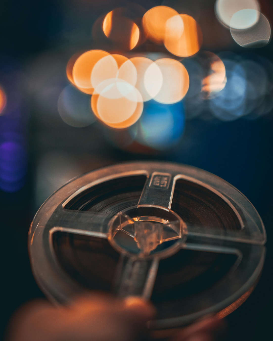 Close-up of a vintage film reel with colorful bokeh lights in the background.