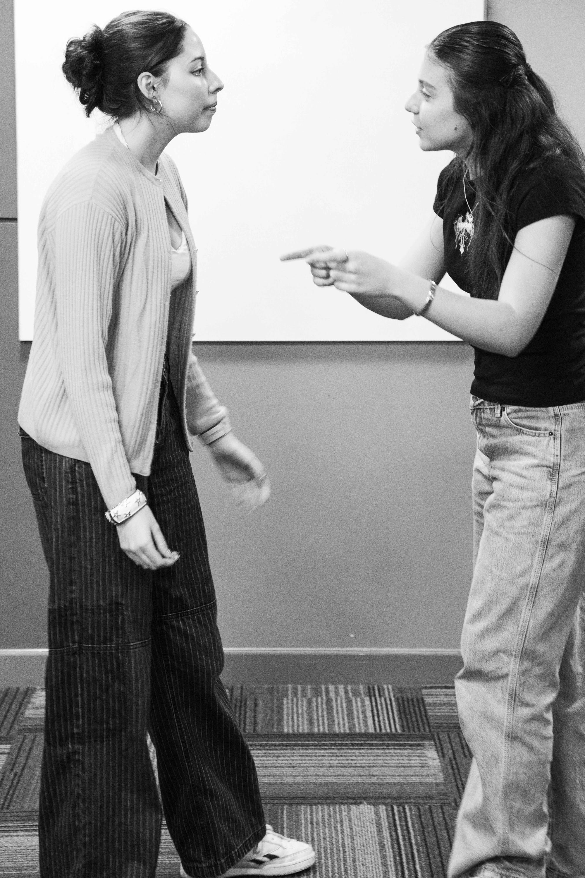 Two women engaged in a heated argument; one woman is pointing finger at the other while she looks on with a calm expression.