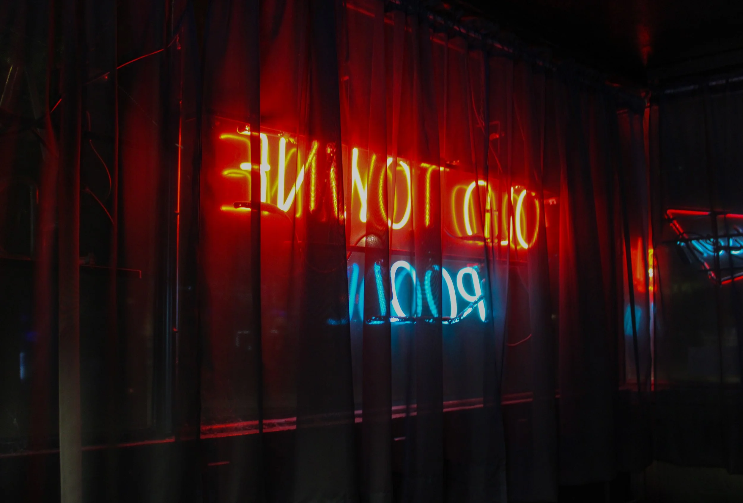 Red and blue neon signs behind a dark curtain.