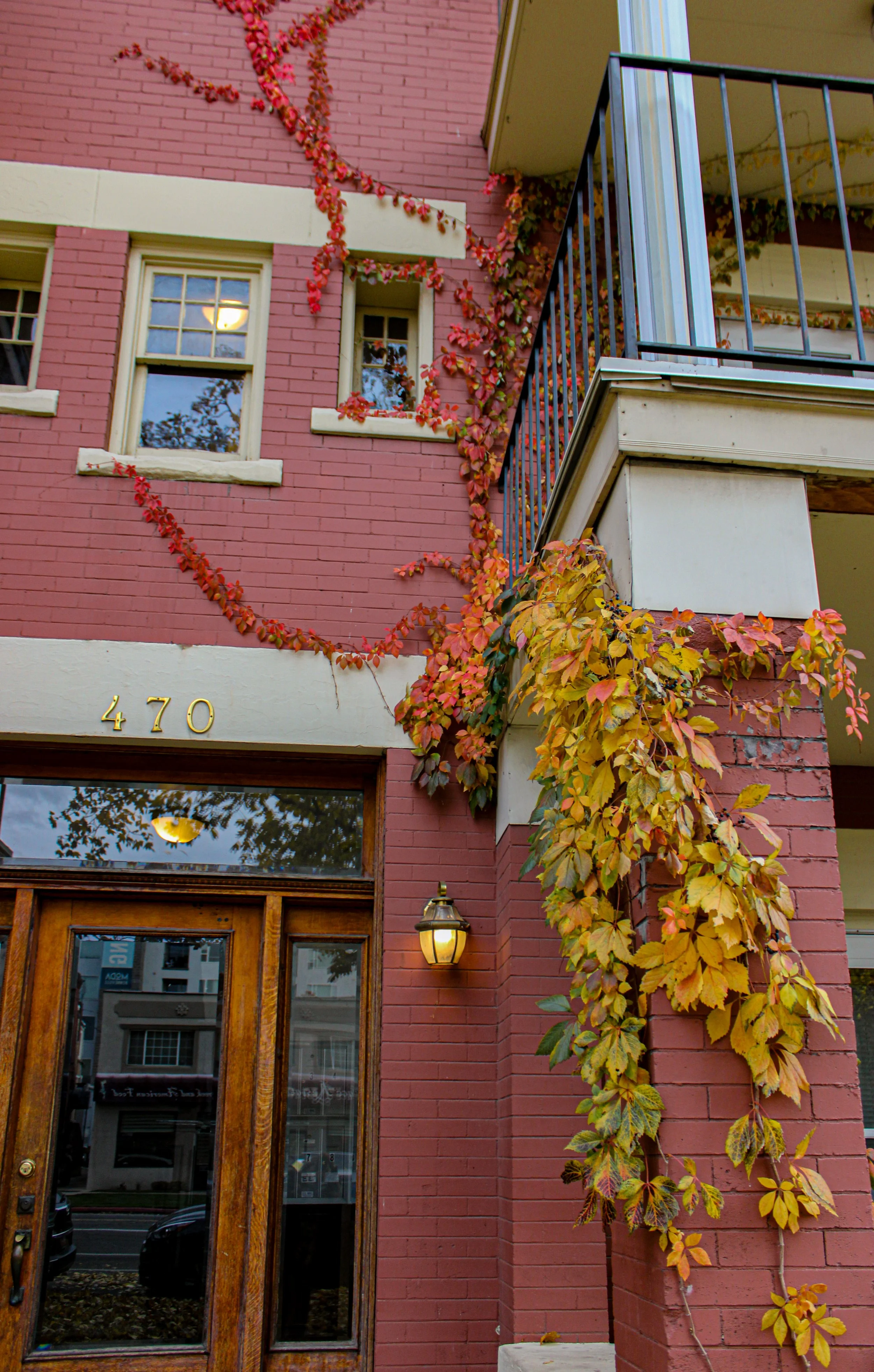 Red brick building with climbing vines, address number 470, and wooden door entrance, with windows and a balcony.