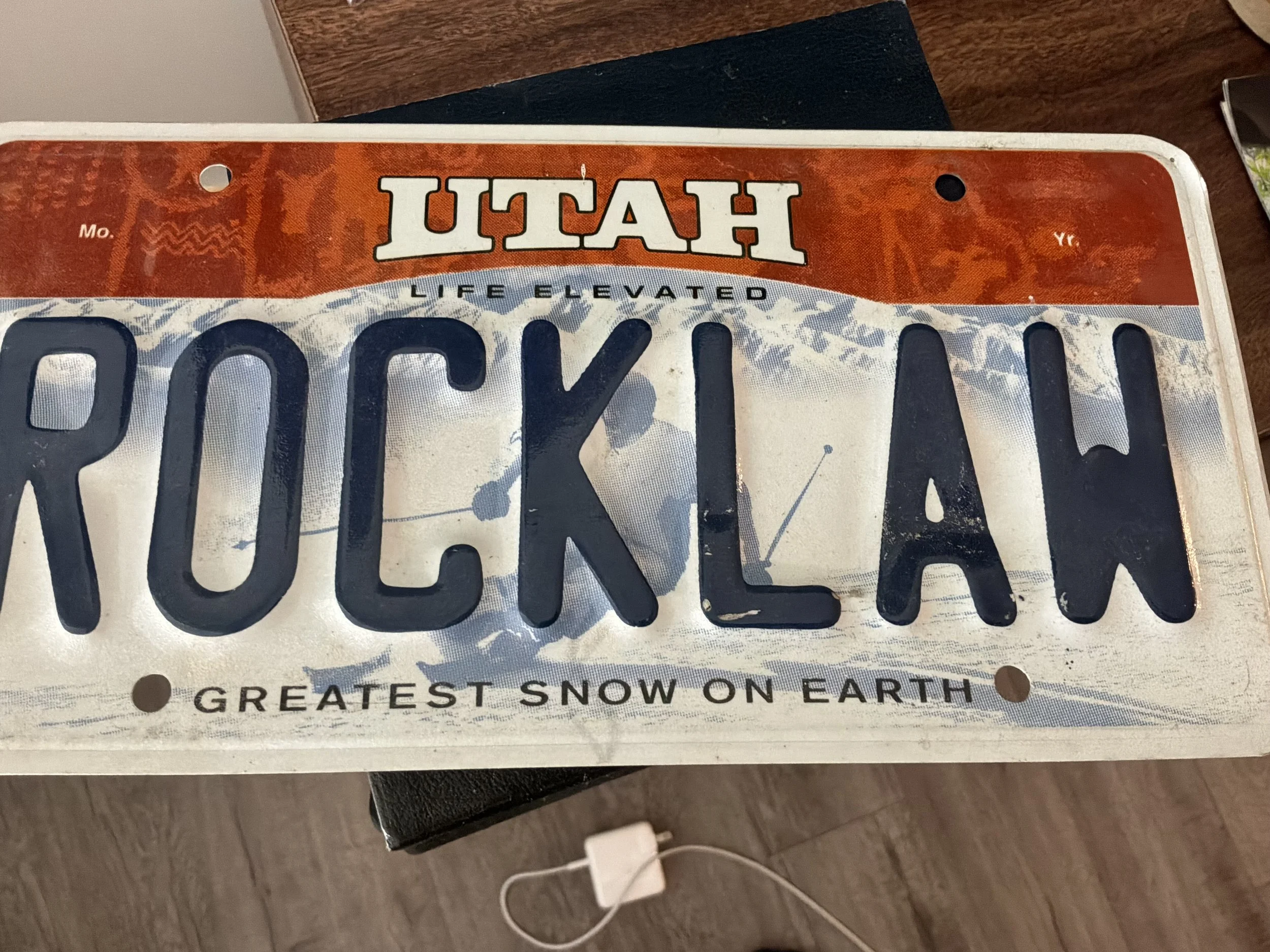 Close-up of a License Plate with the words, 'GREATEST SNOW ON EARTH' visible at the bottom. The license plate reads 'UTAH' at the top and has various orange and white patterns in the background.