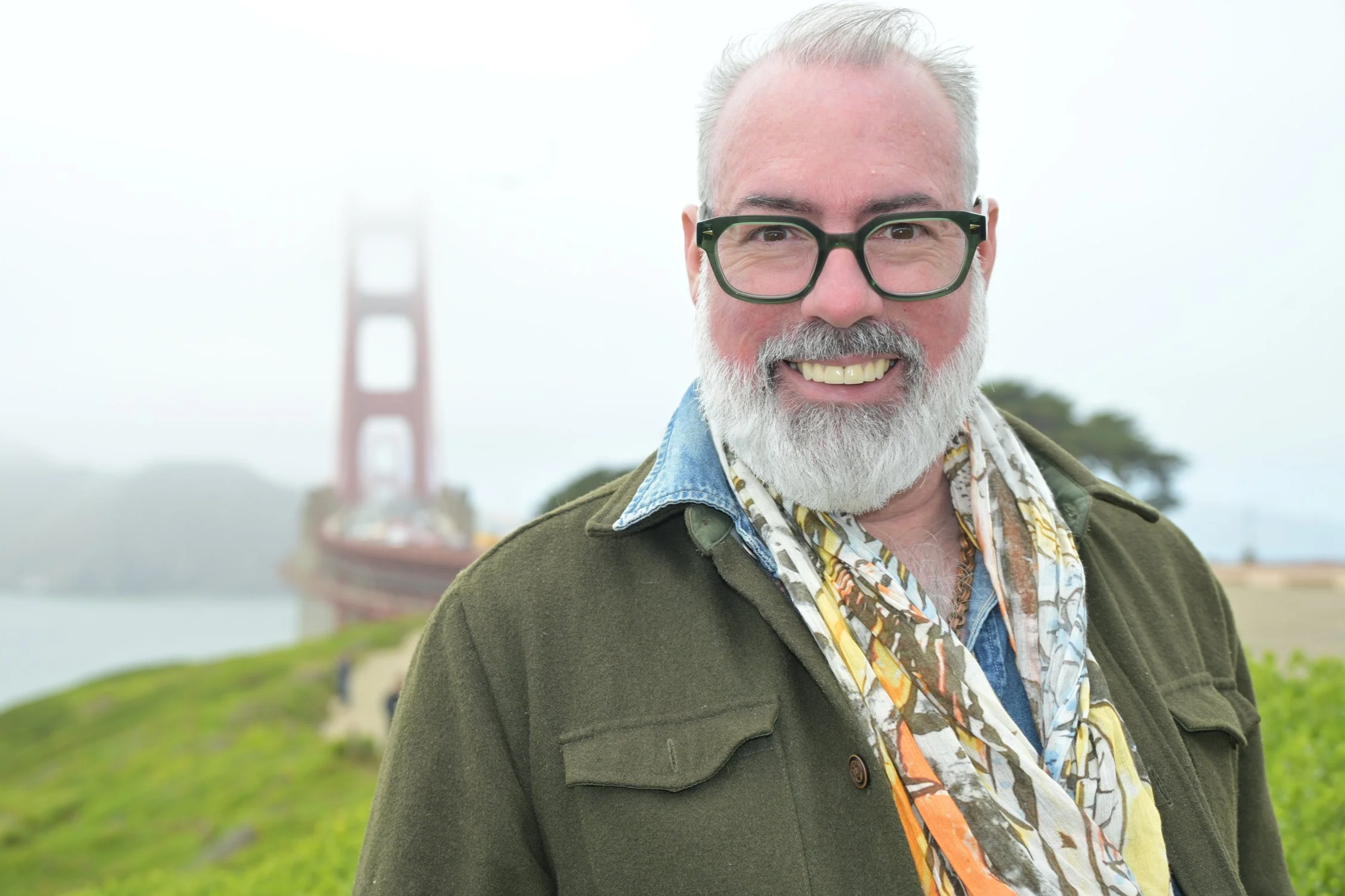 Smiling man with gray hair, beard, and glasses posing outdoors with the Golden Gate Bridge in the background.