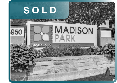 Sold sign on a Madison Park apartment complex sign with a bus stop in front and shrubbery around the base.