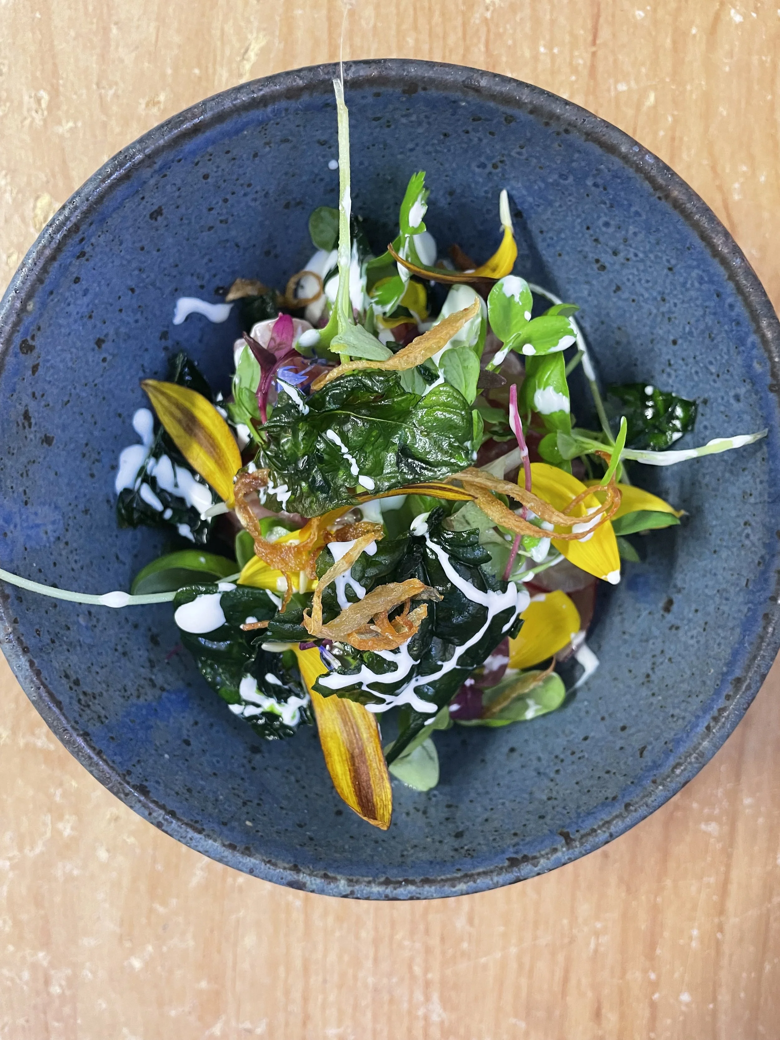 A bowl of mixed greens salad topped with creamy white dressing and crispy fried onions.