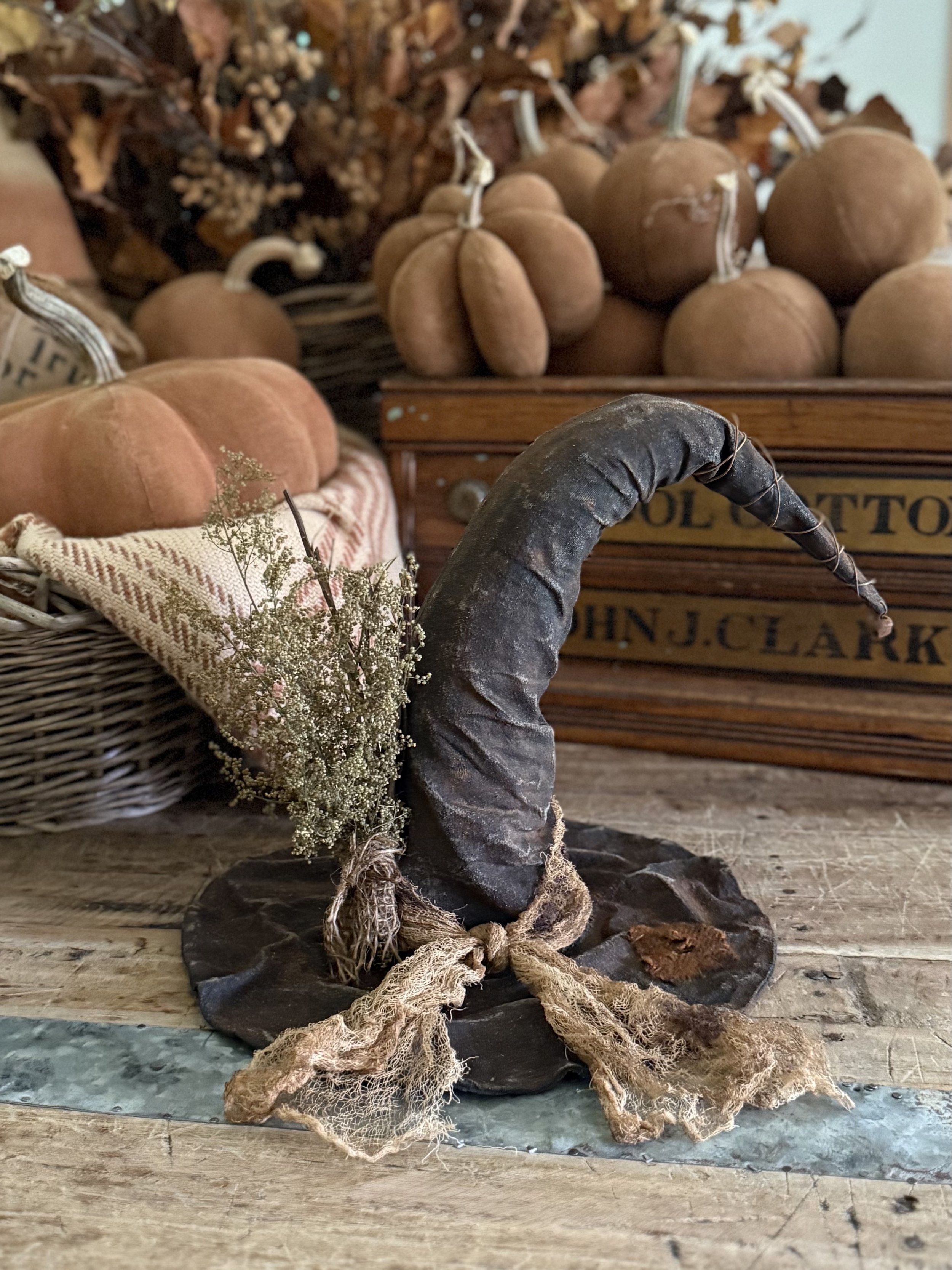 Decorative figurine of a black unicorn horn with a bow, placed on a wooden surface with dried flower accents, in front of baskets of pumpkins and squash in a rustic setting.