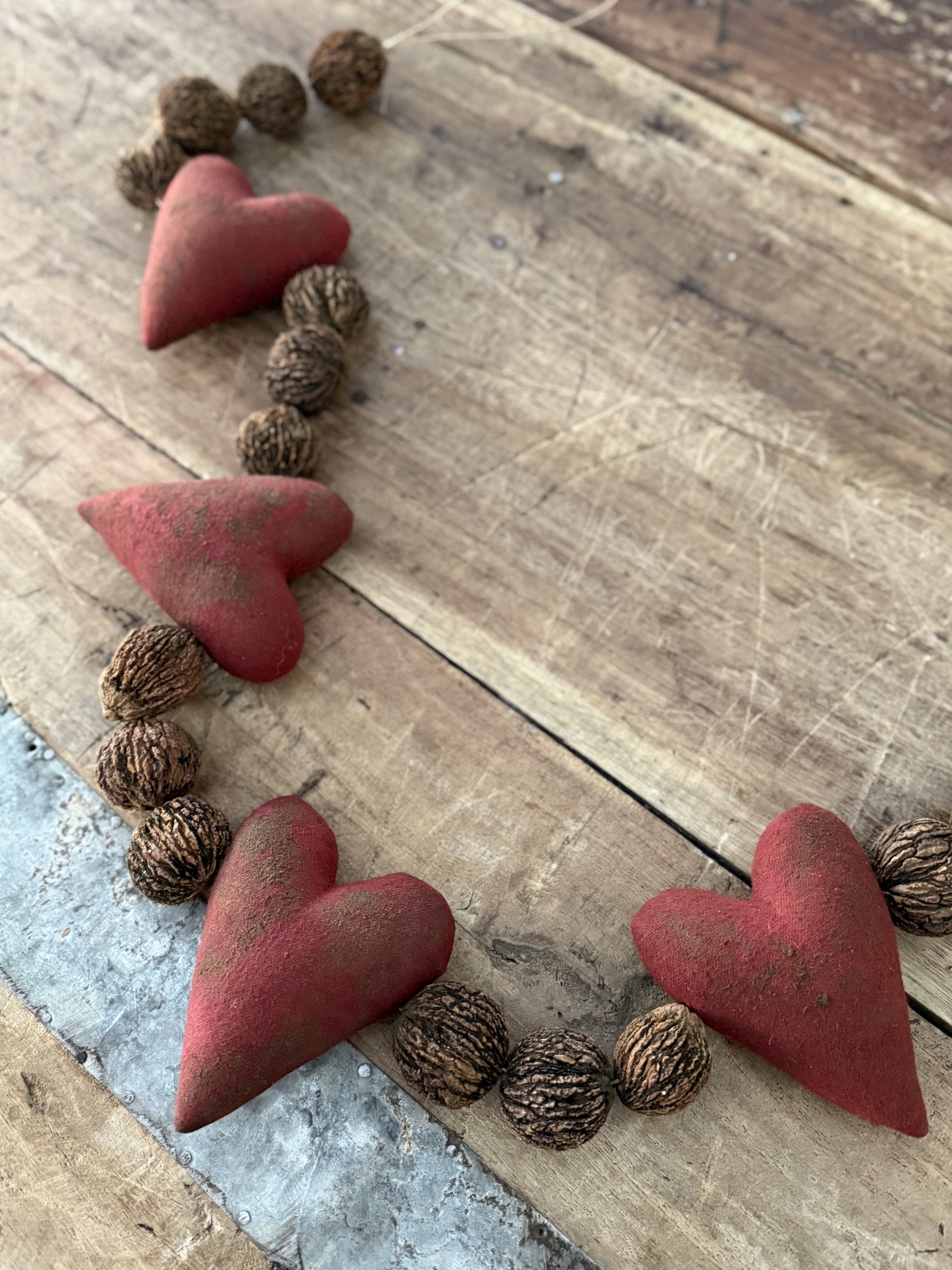 Decorative arrangement of three red fabric hearts and dried seed pods on a wooden surface.