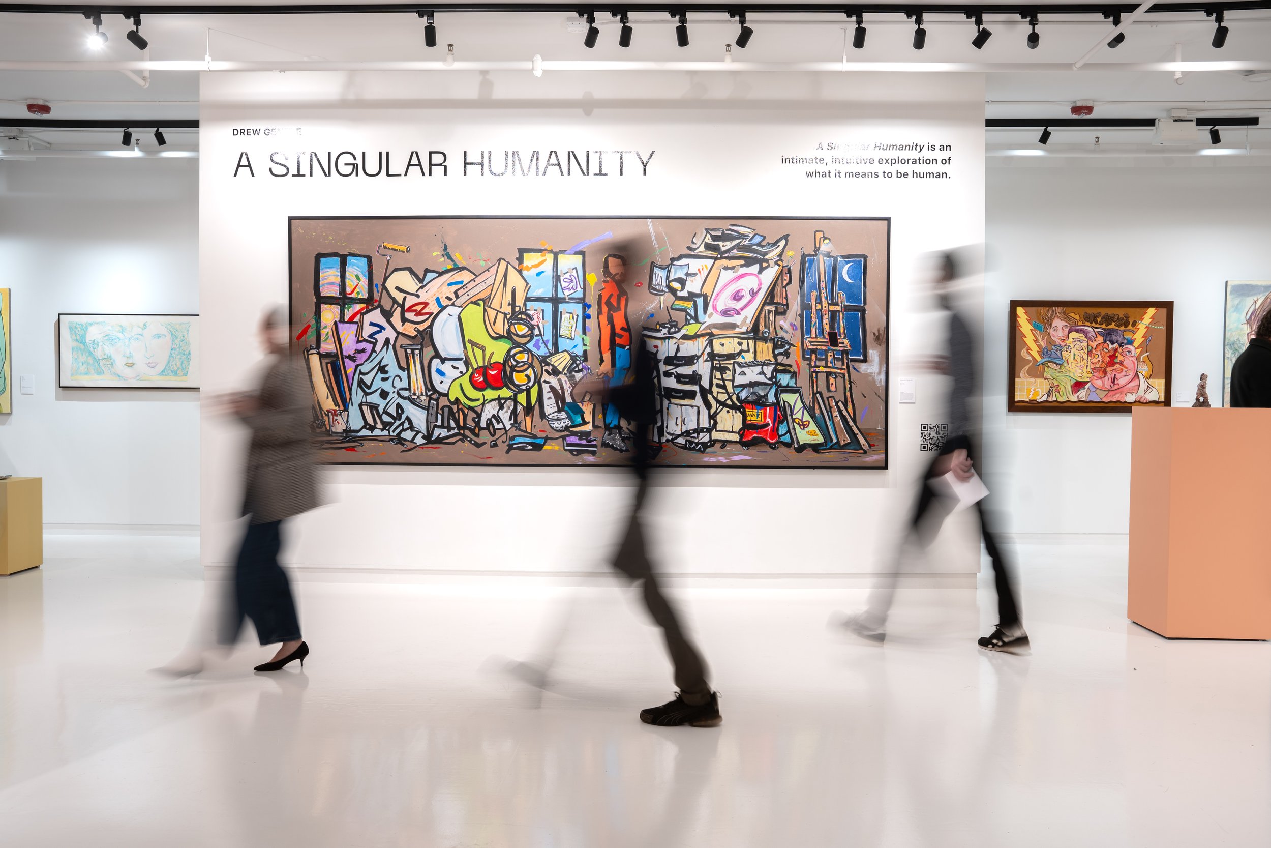 People walking through an art gallery with colorful paintings on the white walls, and the main sign reads, 'A Singular Humanity'.