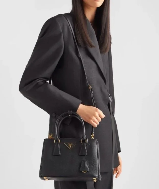 A woman in a black coat holding a black designer handbag with gold accents.