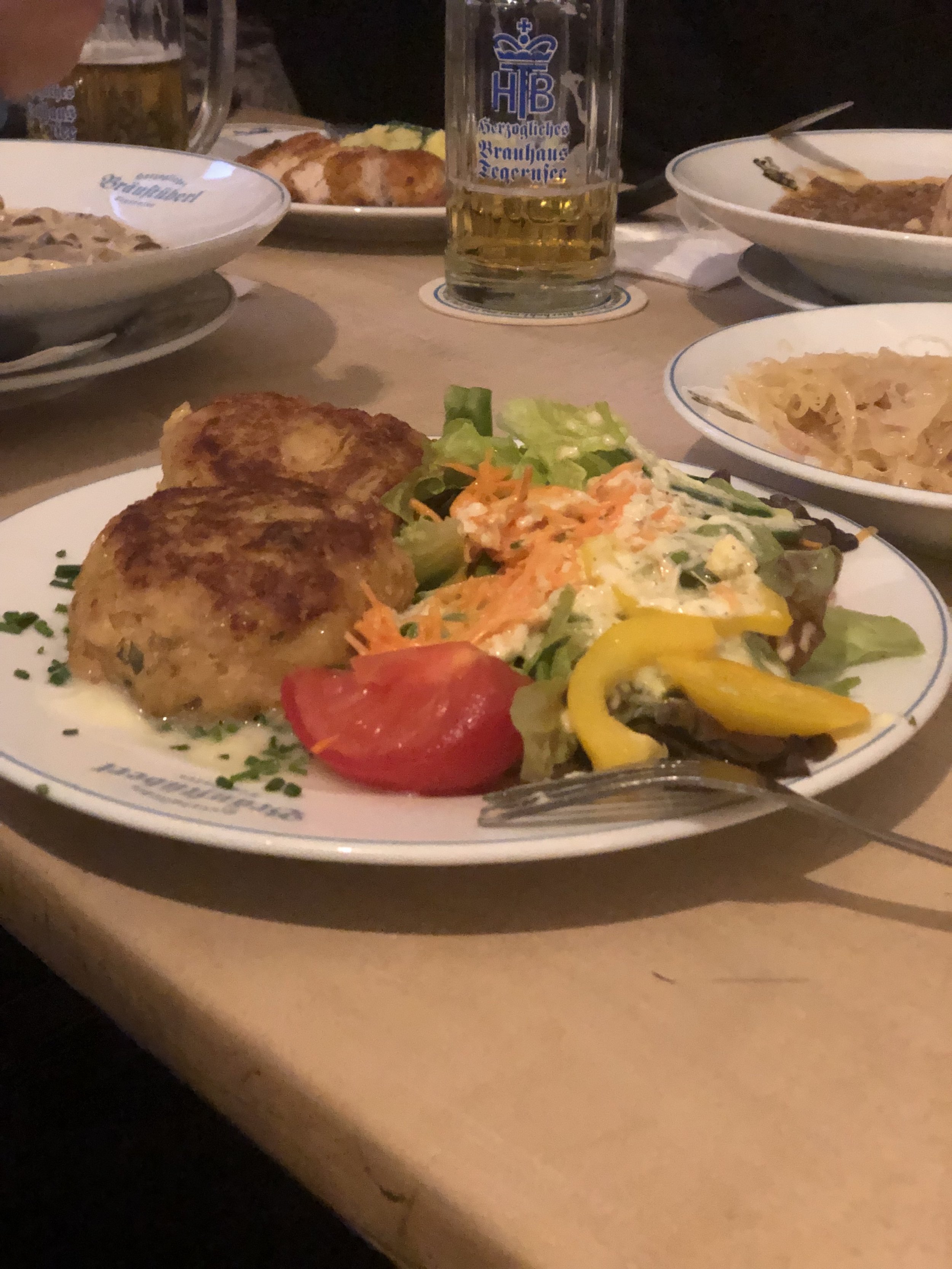 Plate with potato cakes and salad with lettuce, bell peppers, and carrots; glass of beer in background.