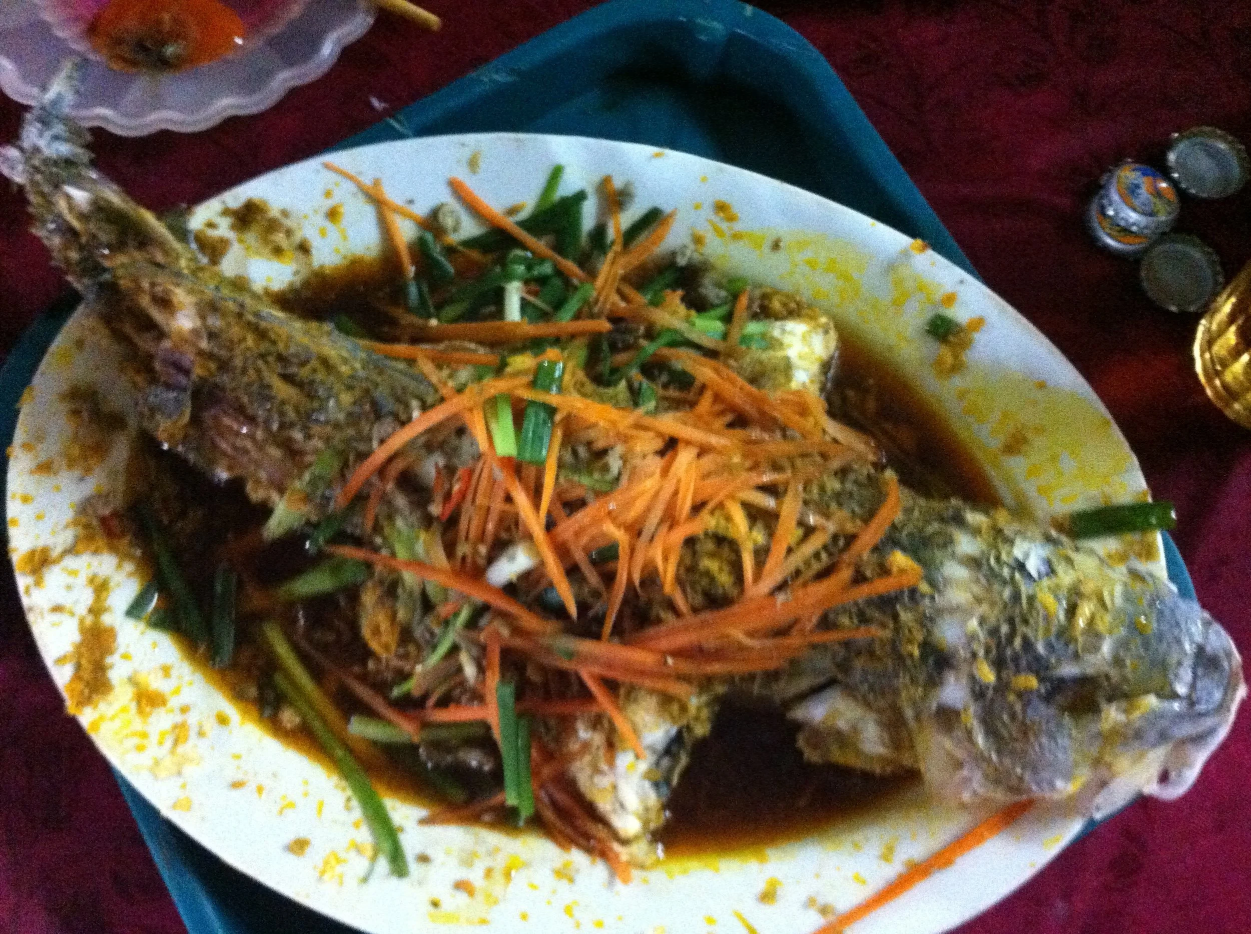 Whole fish cooked in sauce with shredded carrots and green onions on a plate.