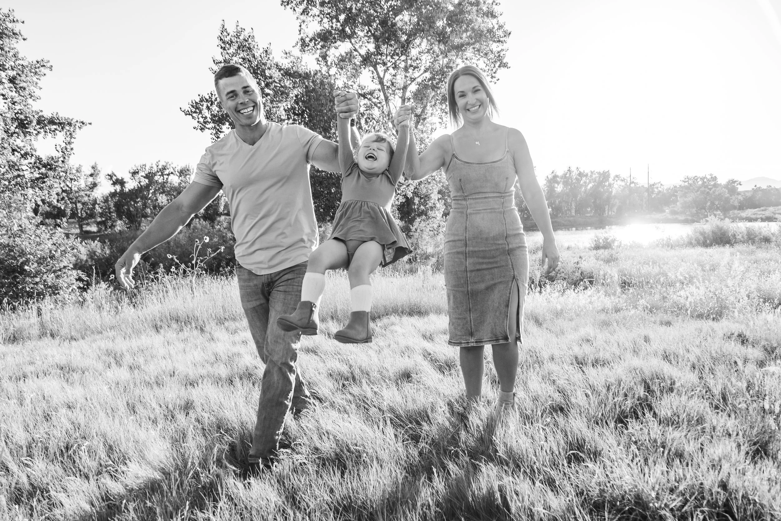 A happy family of three, with a man, woman, and young girl, enjoying a walk in a grassy field during sunset, holding hands and smiling.