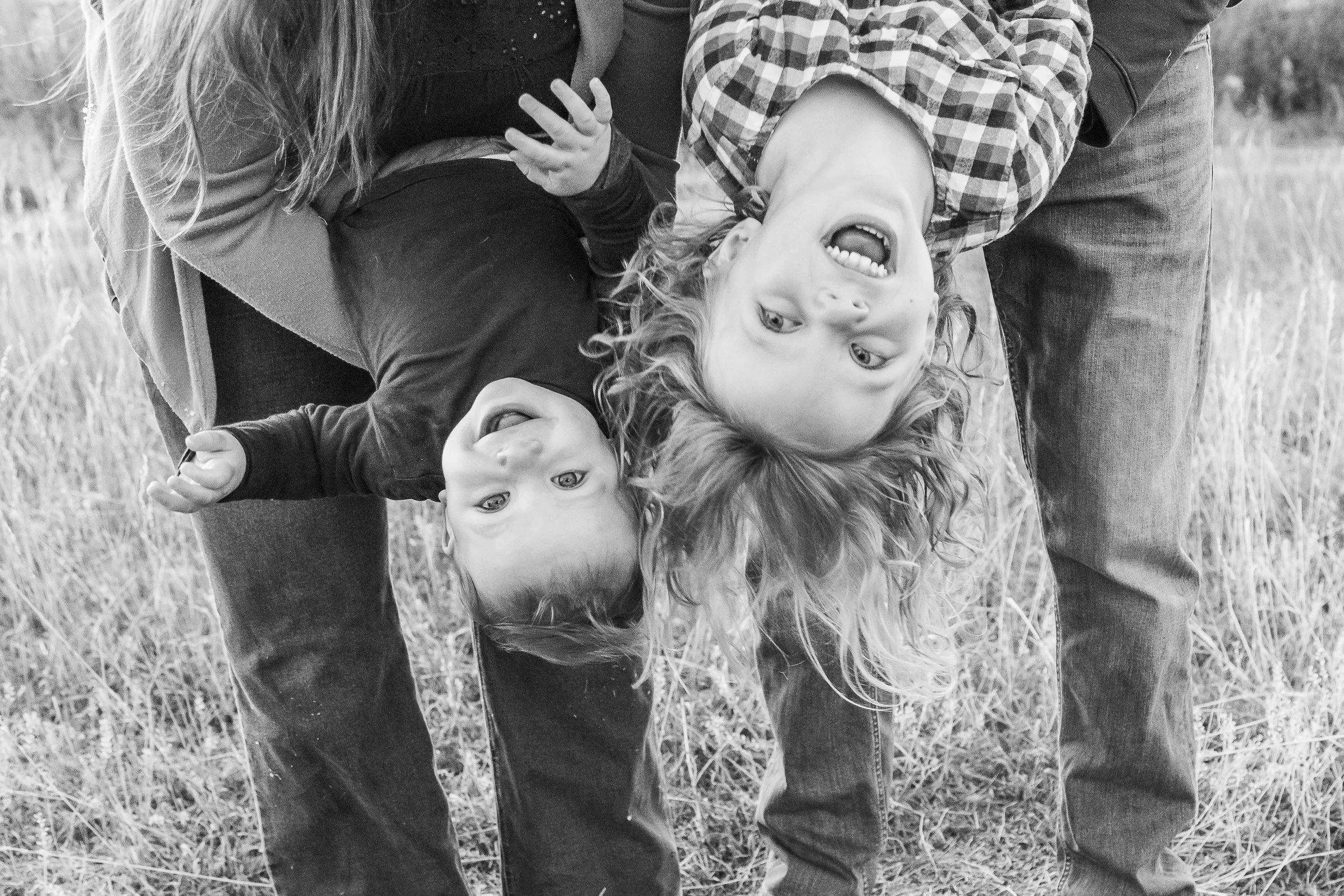 Two children being playful and upside down, lying on the ground outdoors, smiling and laughing