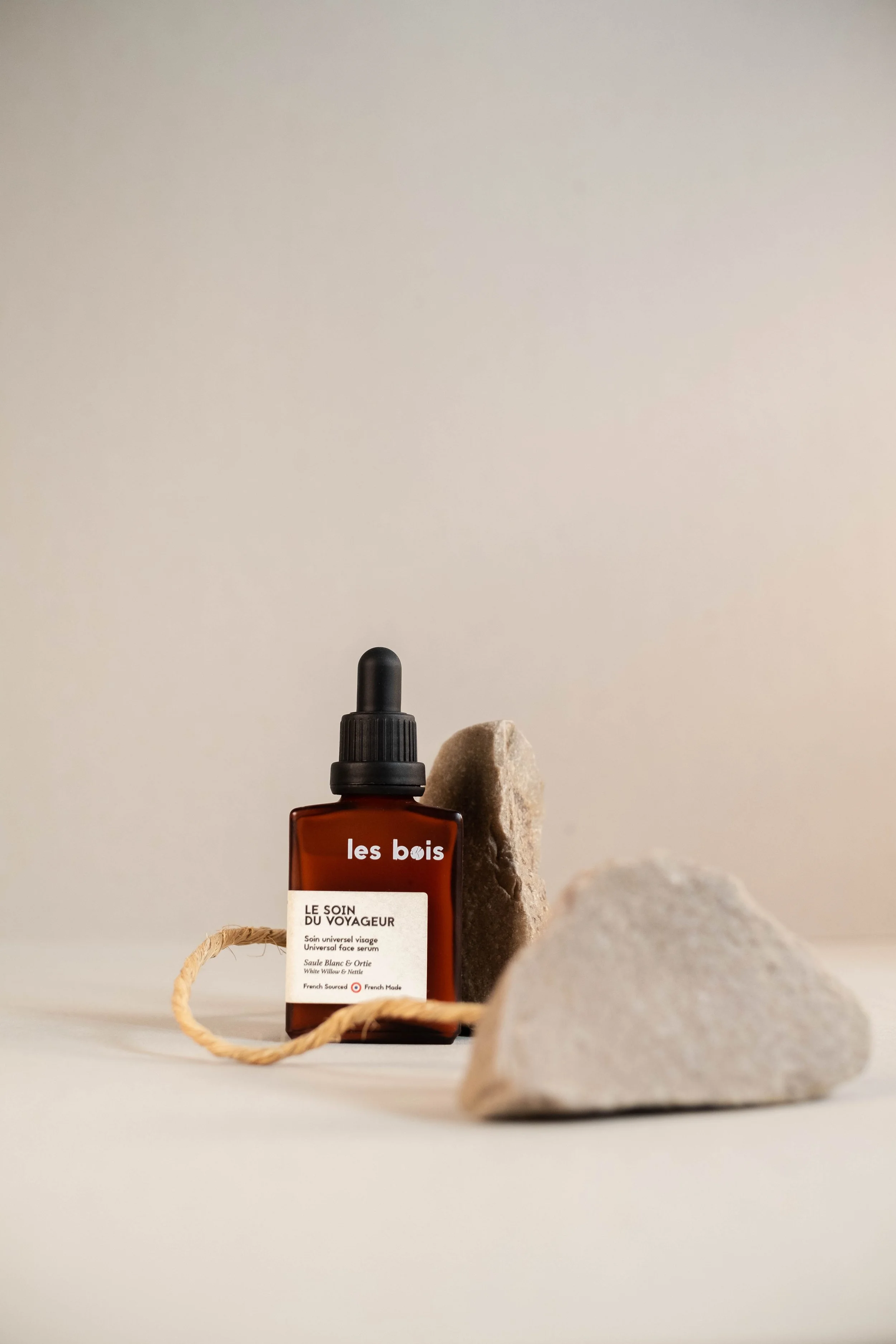 Une bouteille de sérum visage sur fond neutre, entourée de pierres et de corde, avec un style épuré et naturel.