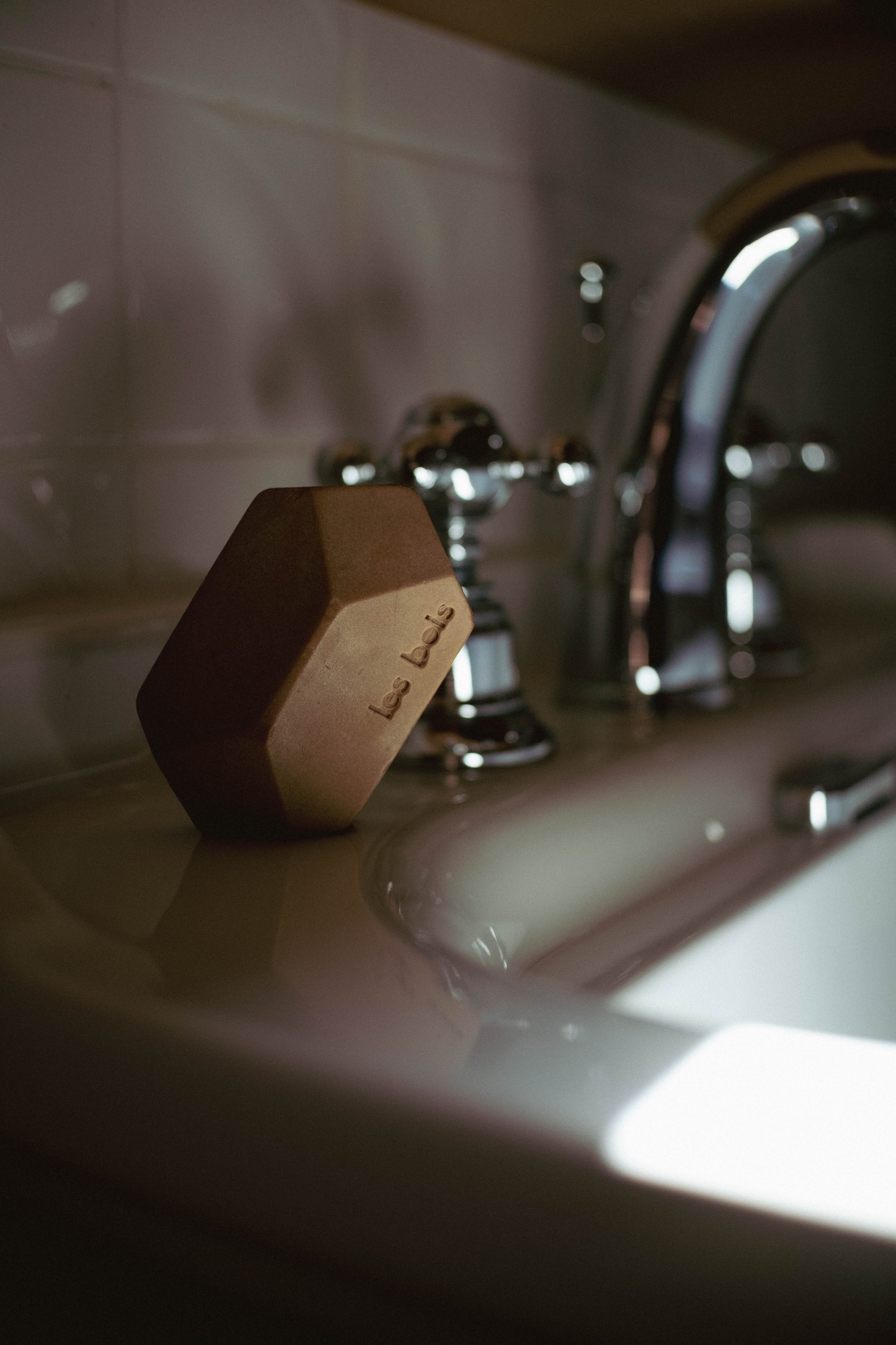 Un savon en forme d'hexagone portant l'inscription "les savons" posé sur un évier en porcelaine près d'un robinet en métal chromé.