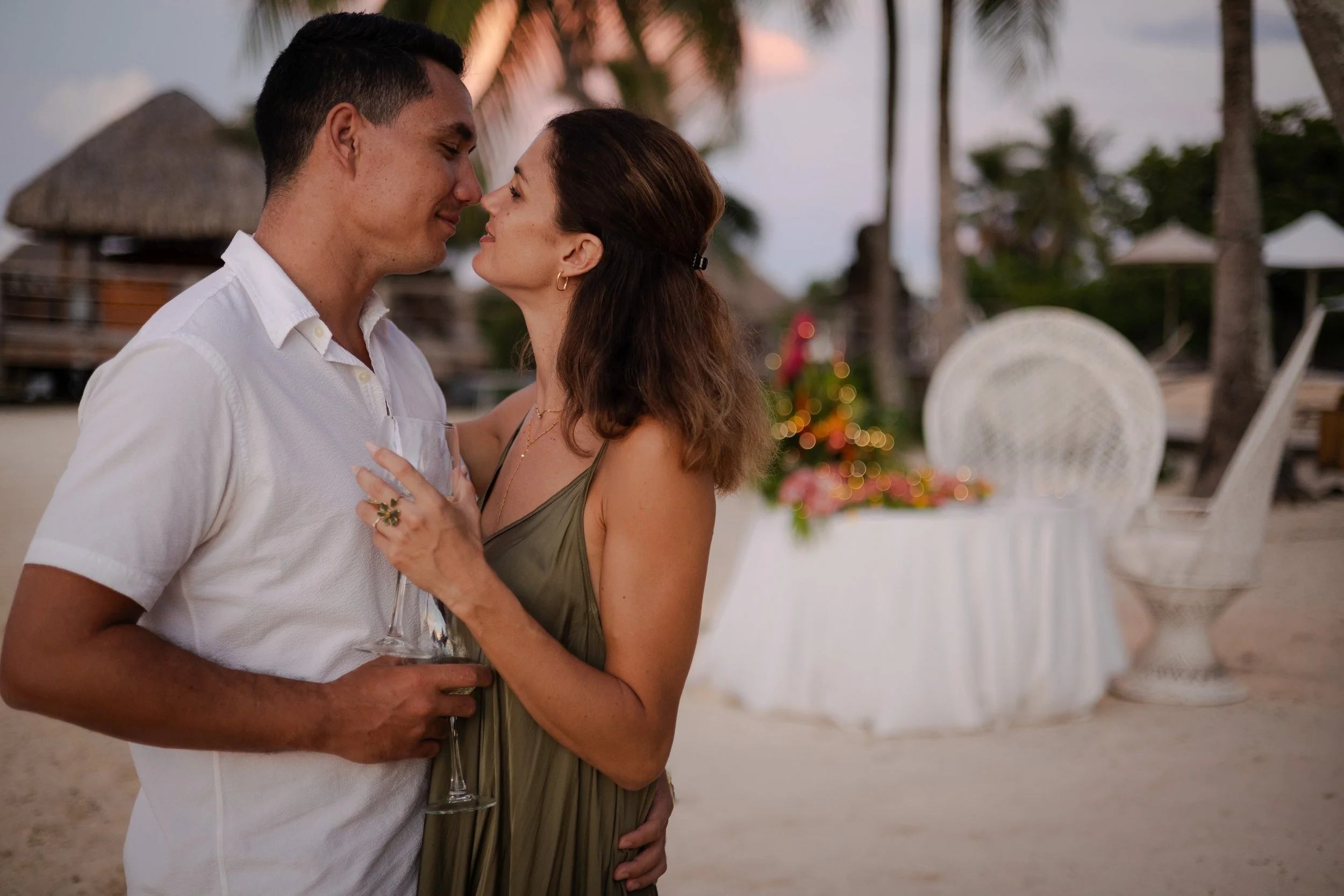 Un couple s'apprête à s'embrasser sur la plage au coucher du soleil, avec une décoration de Noël en arrière-plan.