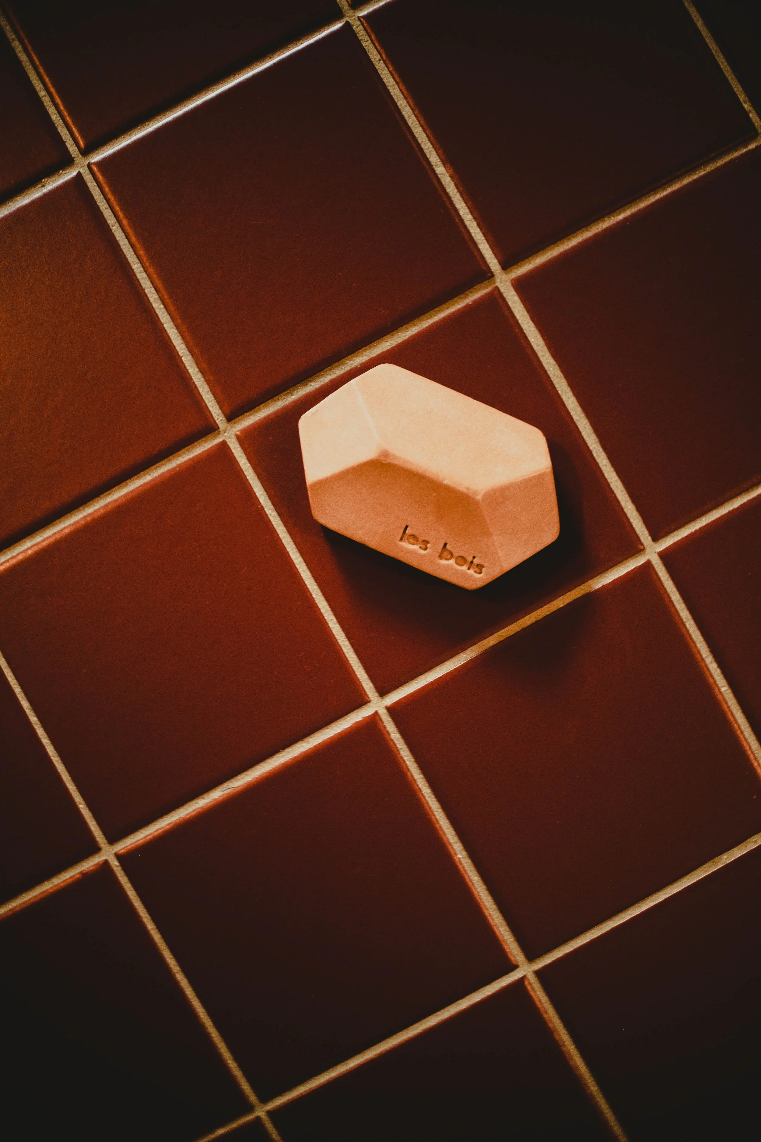 Un morceau de savon en forme de cône posé sur des carreaux de salle de bain bruns.