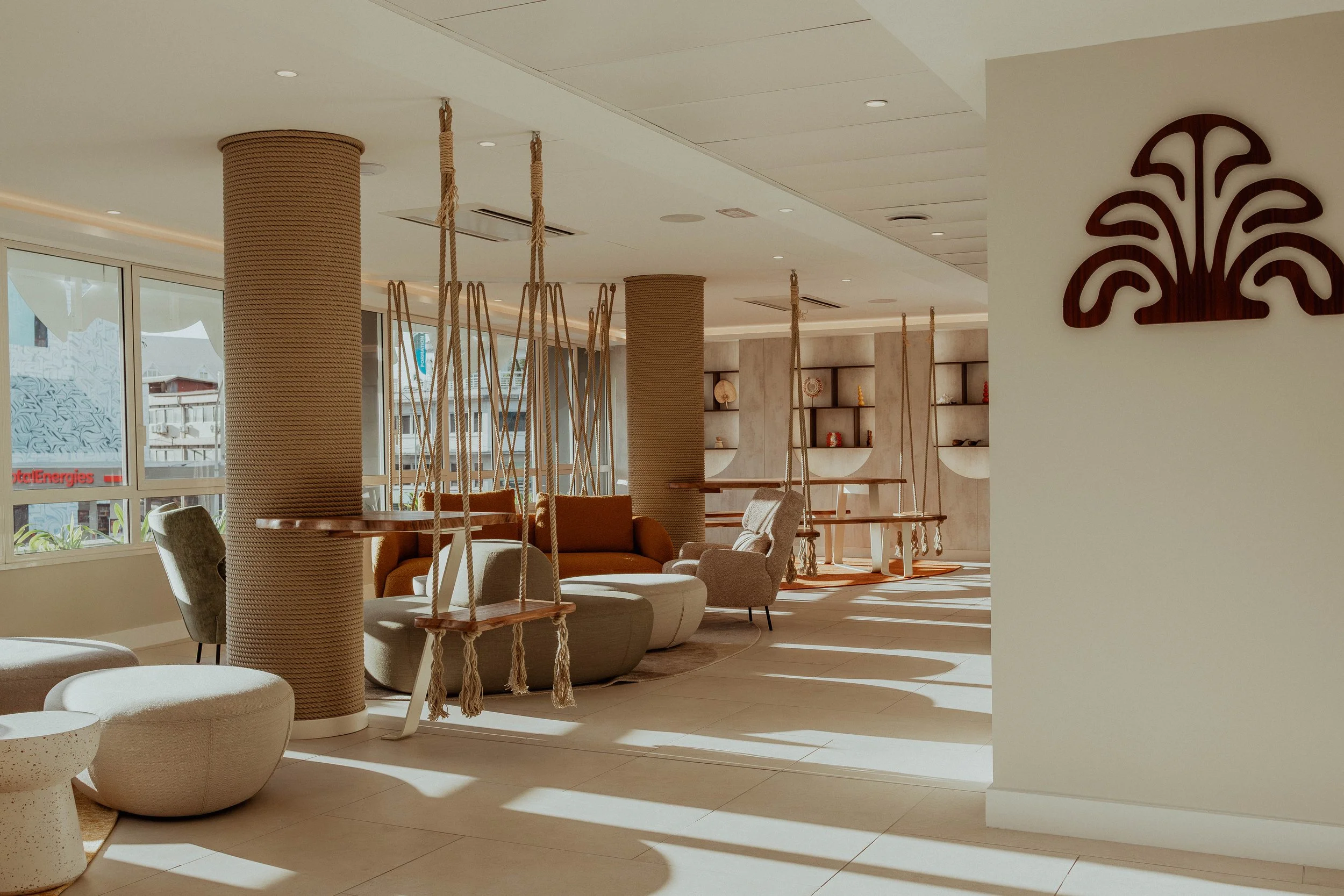Intérieur moderne d'un hall avec des balançoires en bois suspendues, un canapé orange, des fauteuils et des étagères décoratives, en pleine lumière naturelle.