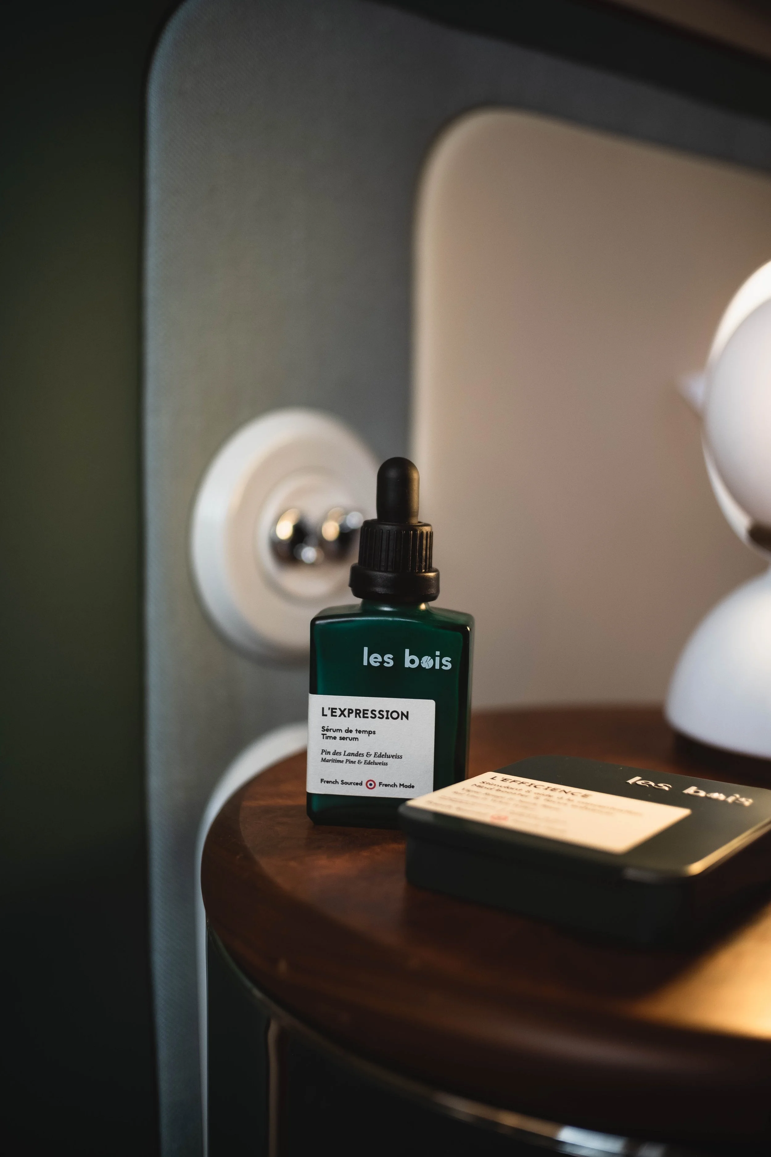 Un flacon de sérum appelé 'L'EXPRESSION' posé sur une table en bois foncé, à côté d'une boîte portant le même nom.