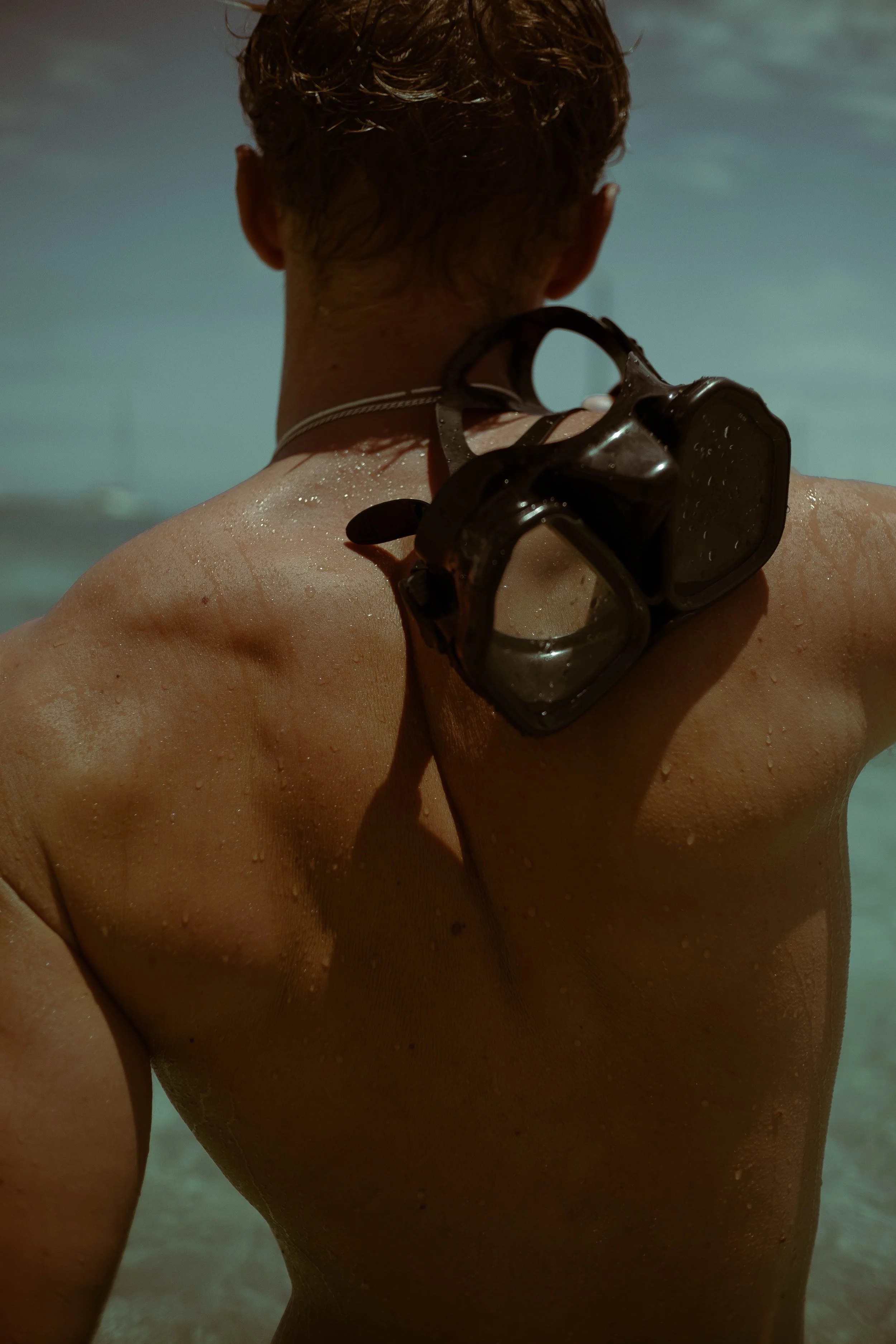 Un homme vu de dos, portant un masque de plongée sur l'épaule, avec de la sueur ou de l'eau sur le dos dans un environnement aquatique.