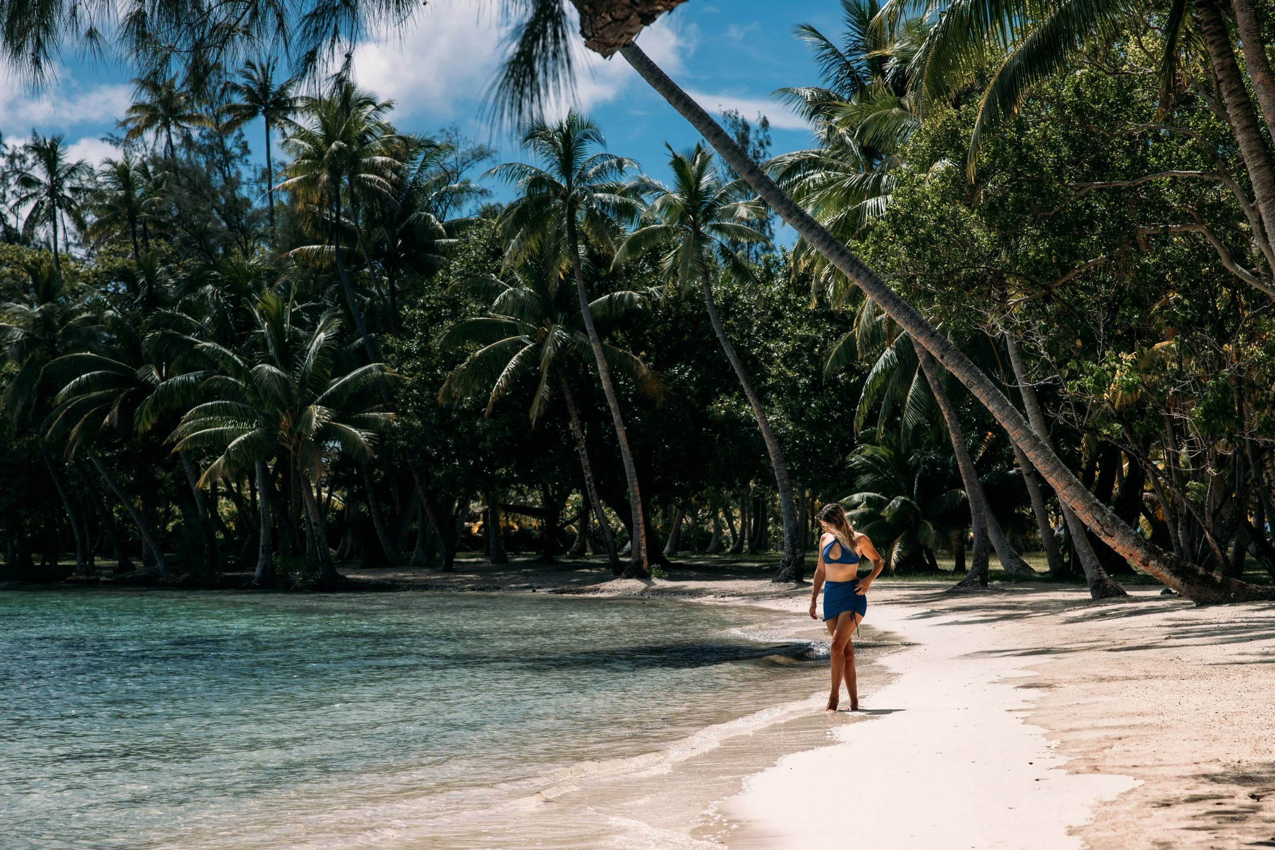 Femme marchant sur une plage de sable blanc avec des palmiers et un ciel bleu