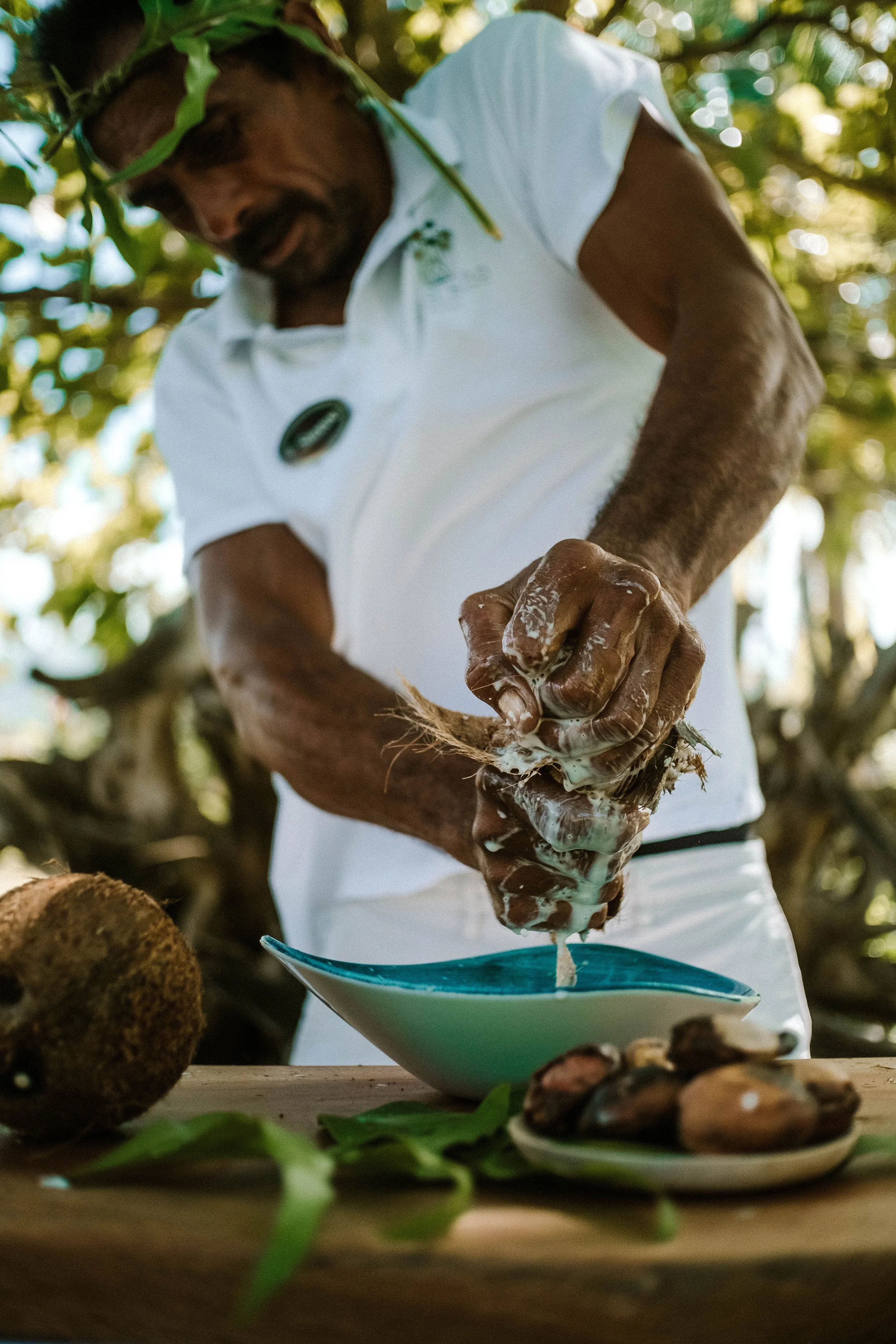 Homme préparant des fruits de mer dans un environnement naturel avec des feuilles vertes autour.