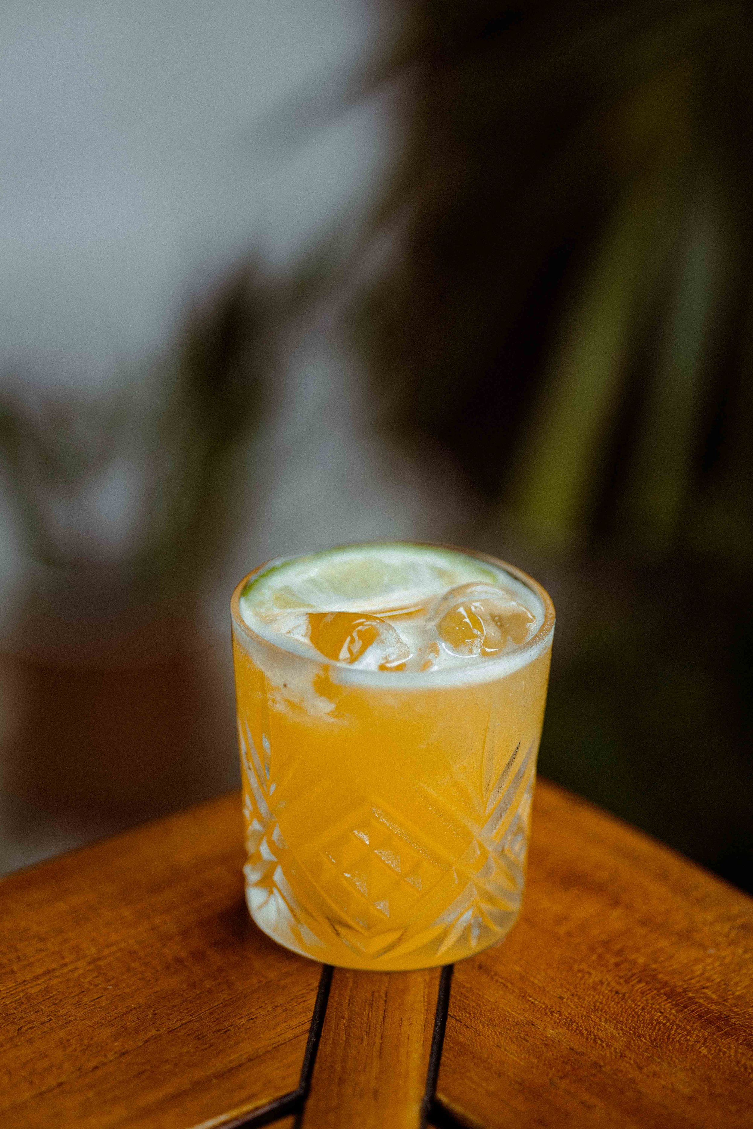 Un verre de cocktail orange avec glaçons, servi avec une tranche de citron vert, posé sur une table en bois.