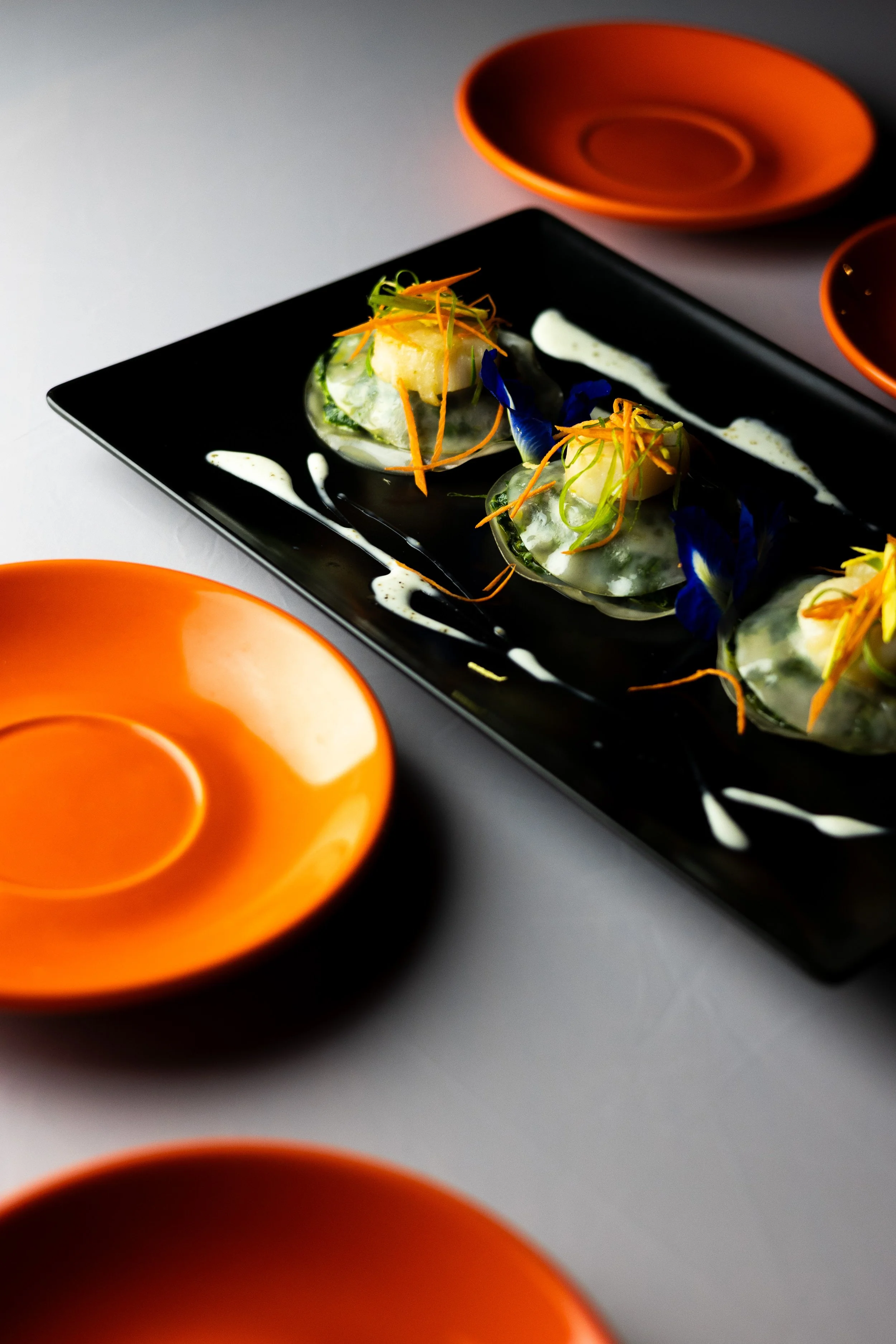 Assiette de sushi garnie de légumes et fleurs comestibles, servie sur une assiette noire, entourée de bols orange