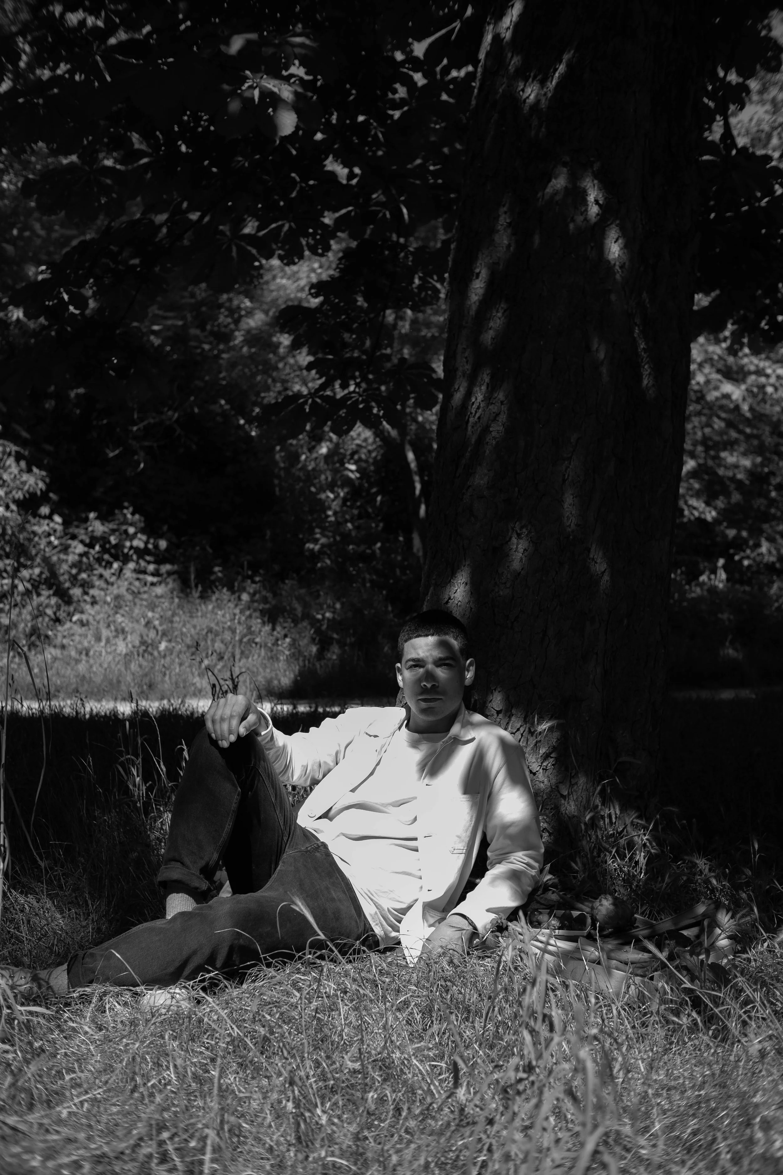 Un homme assis par terre sous un arbre, dans un environnement naturel.