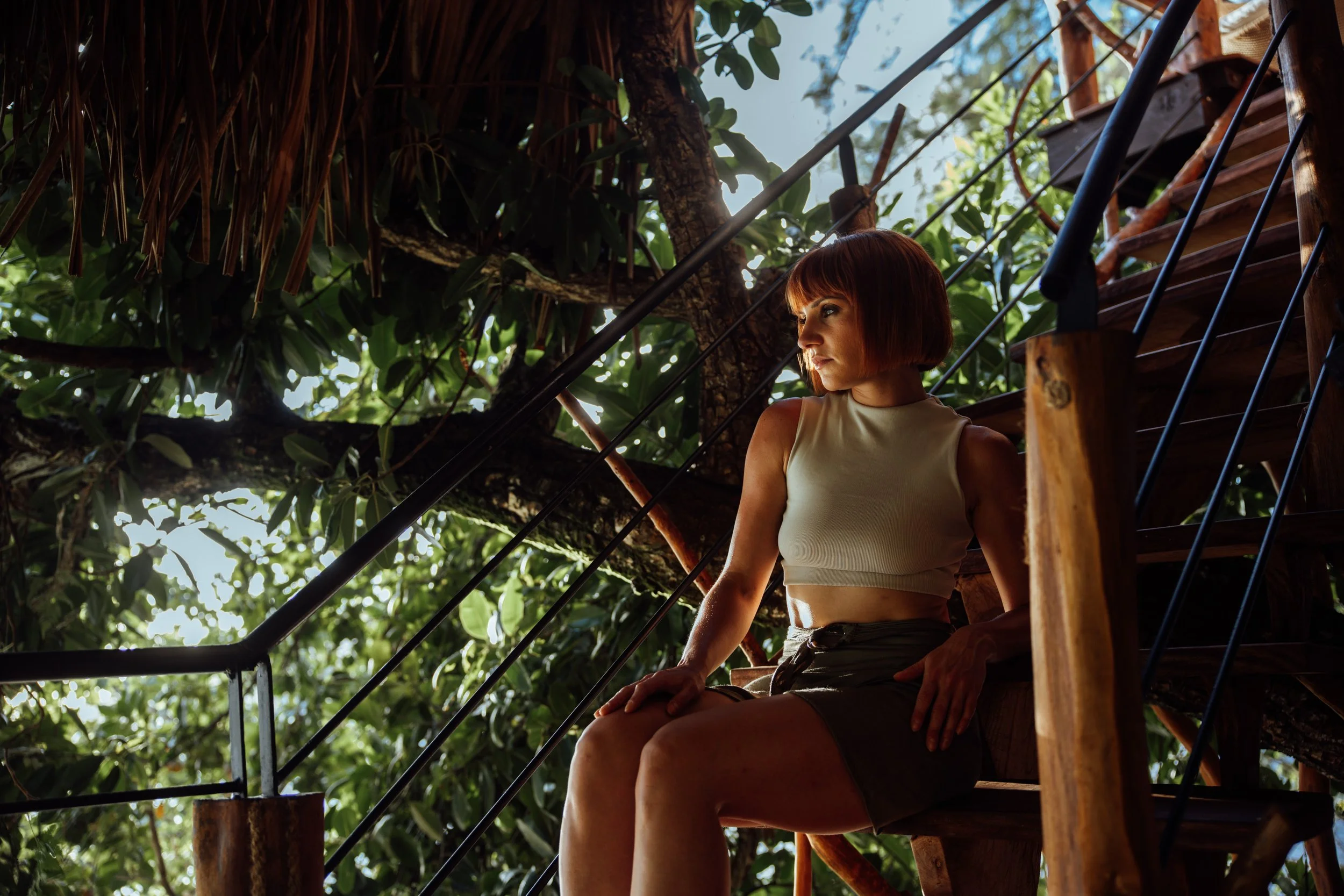 Femme assise sur un escalier en bois dans un environnement forestier avec beaucoup de feuillage.