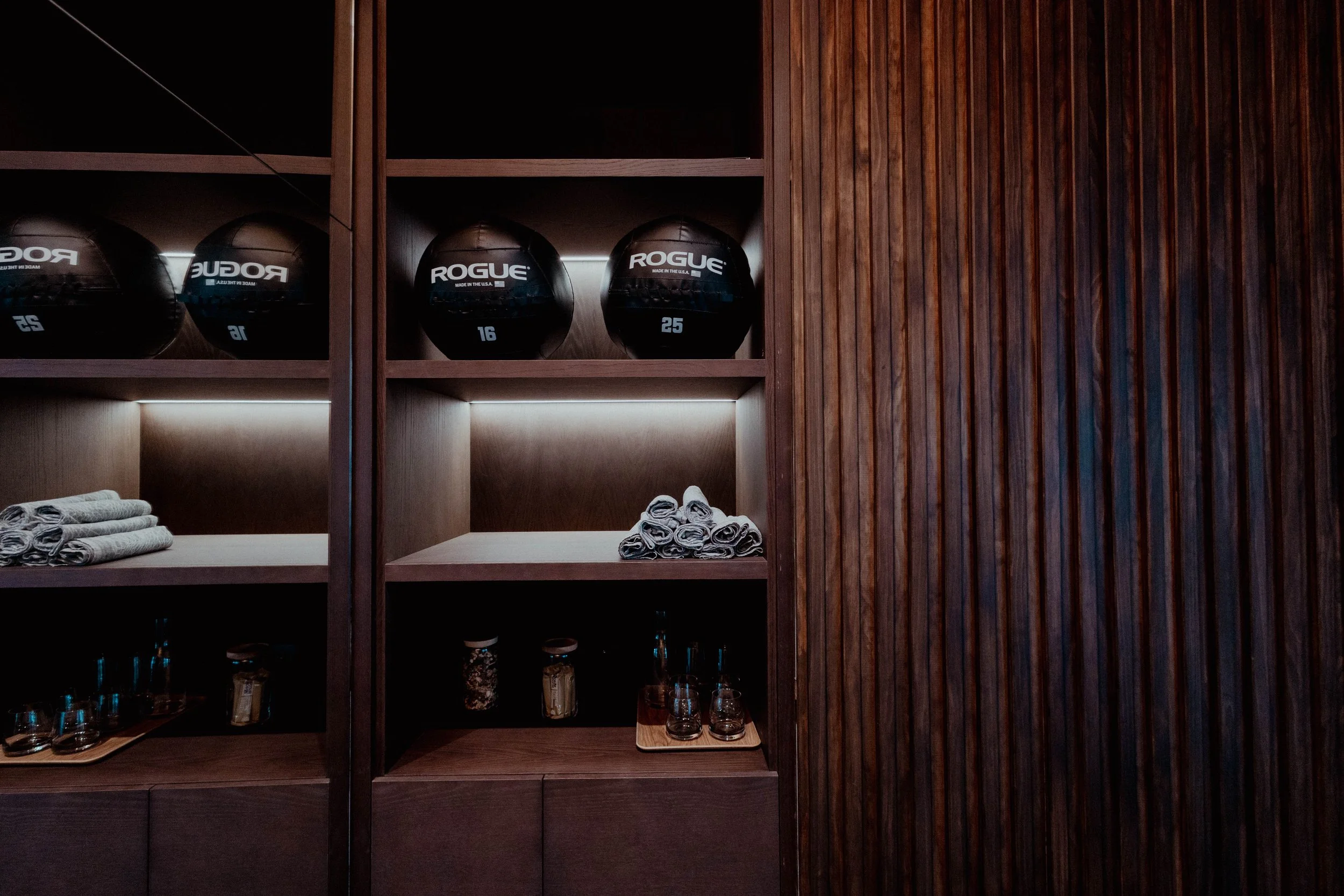 Étagère en bois avec balles de fitness Rogue, serviettes et verres dans une salle de sport ou de yoga.