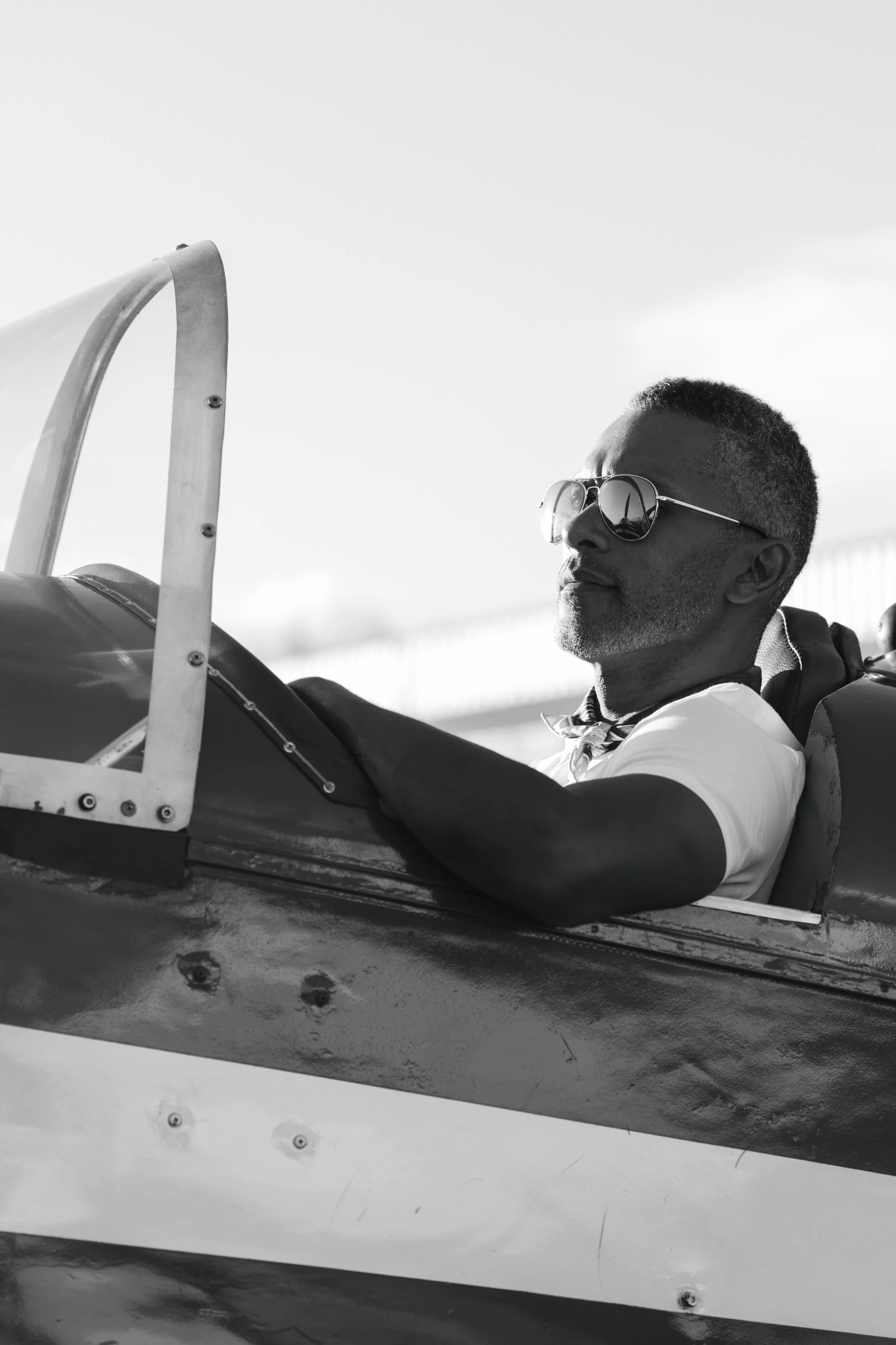 Un homme portant des lunettes de soleil assis dans un cockpit d'avion ou de planeur en noir et blanc.