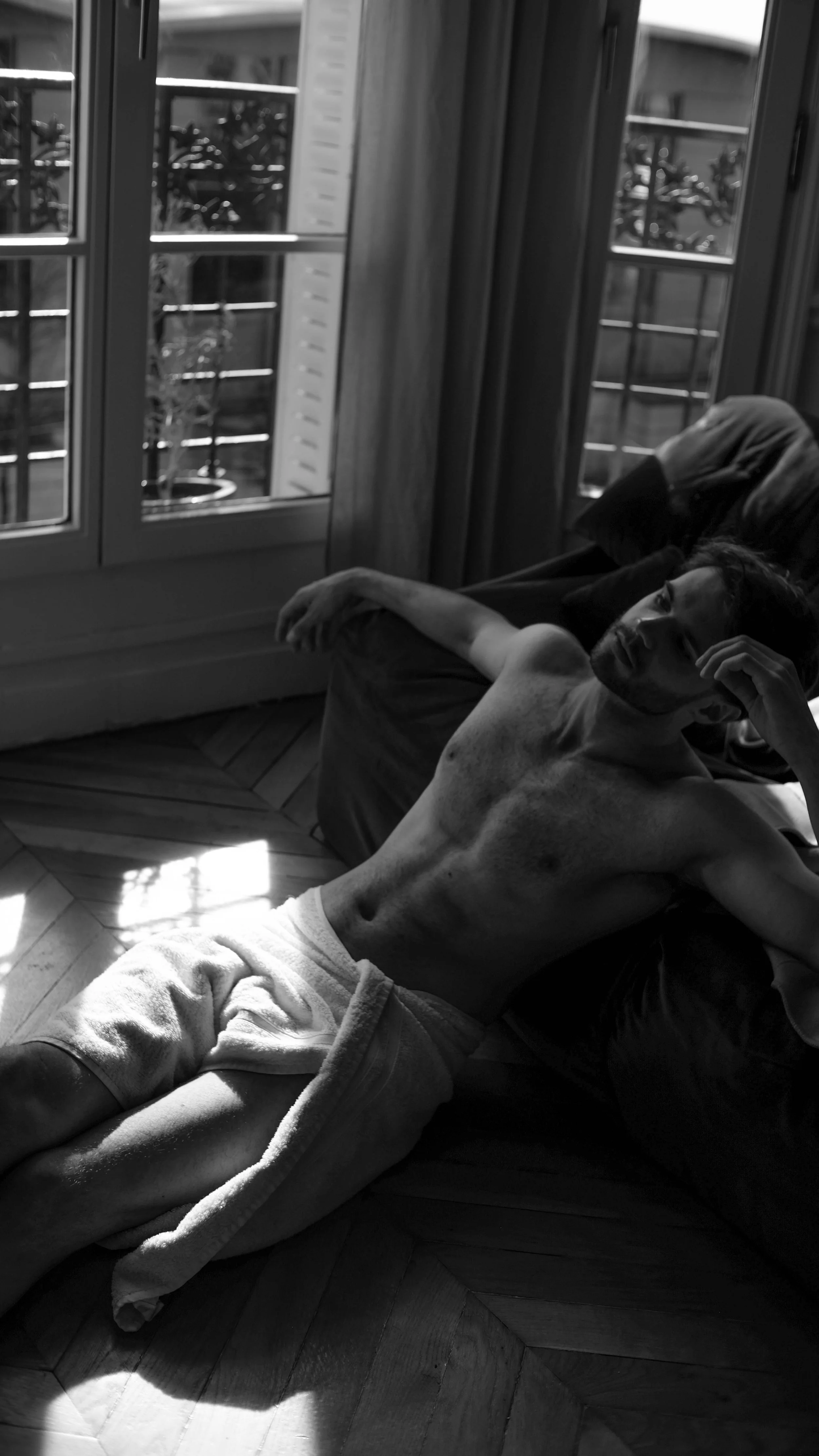 Jeune homme allongé sur un sofa près d'une fenêtre, en lumière naturelle.