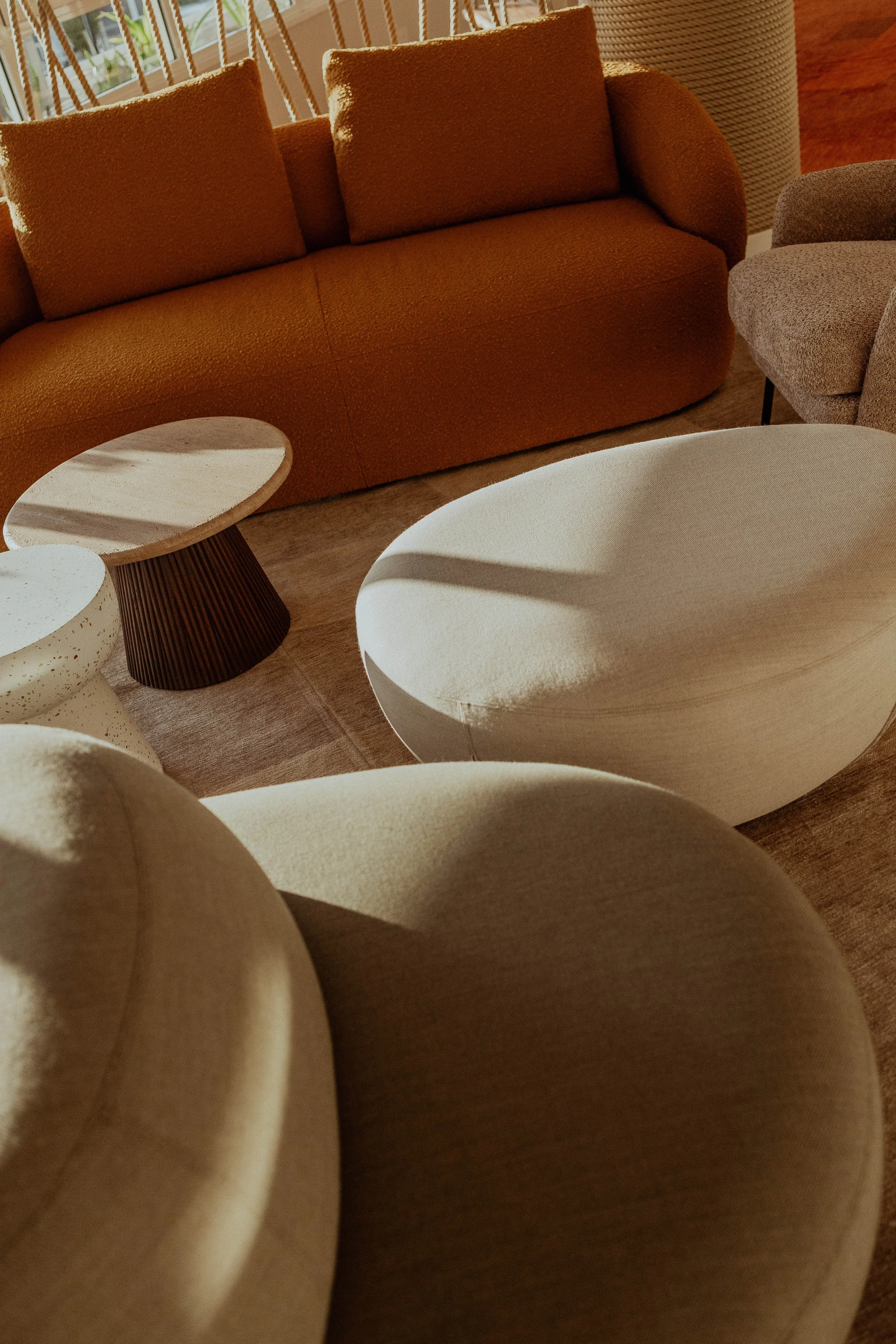 Salon avec un canapé marron, un fauteuil gris, deux tables basses en forme de coupe, et un tapis beige, dans une pièce lumineuse avec des fenêtres.