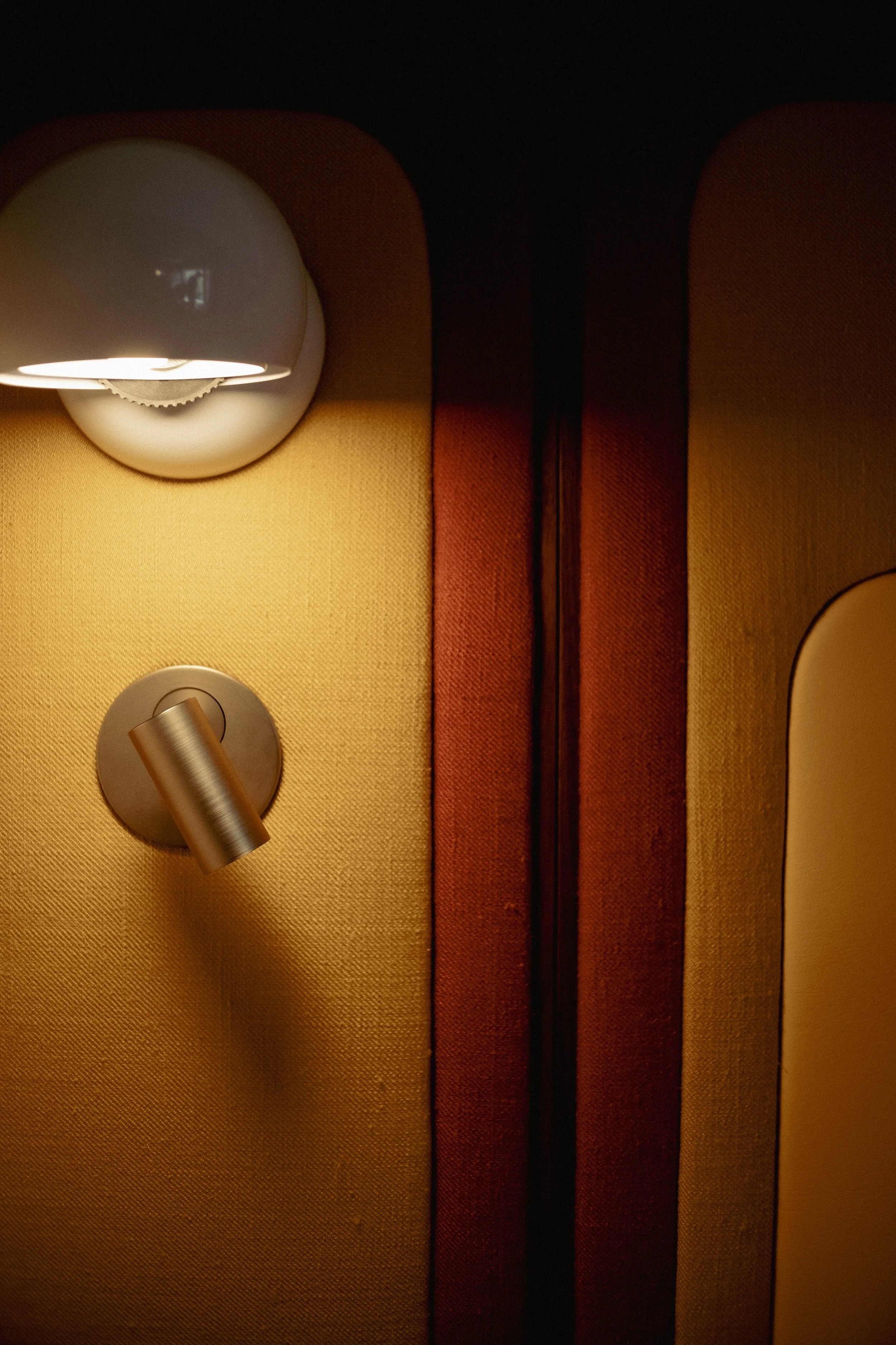 Deux appliques murales, une demi-boule blanche et une autre cylindrique, fixées sur un mur recouvert de tissu jaune et orange.