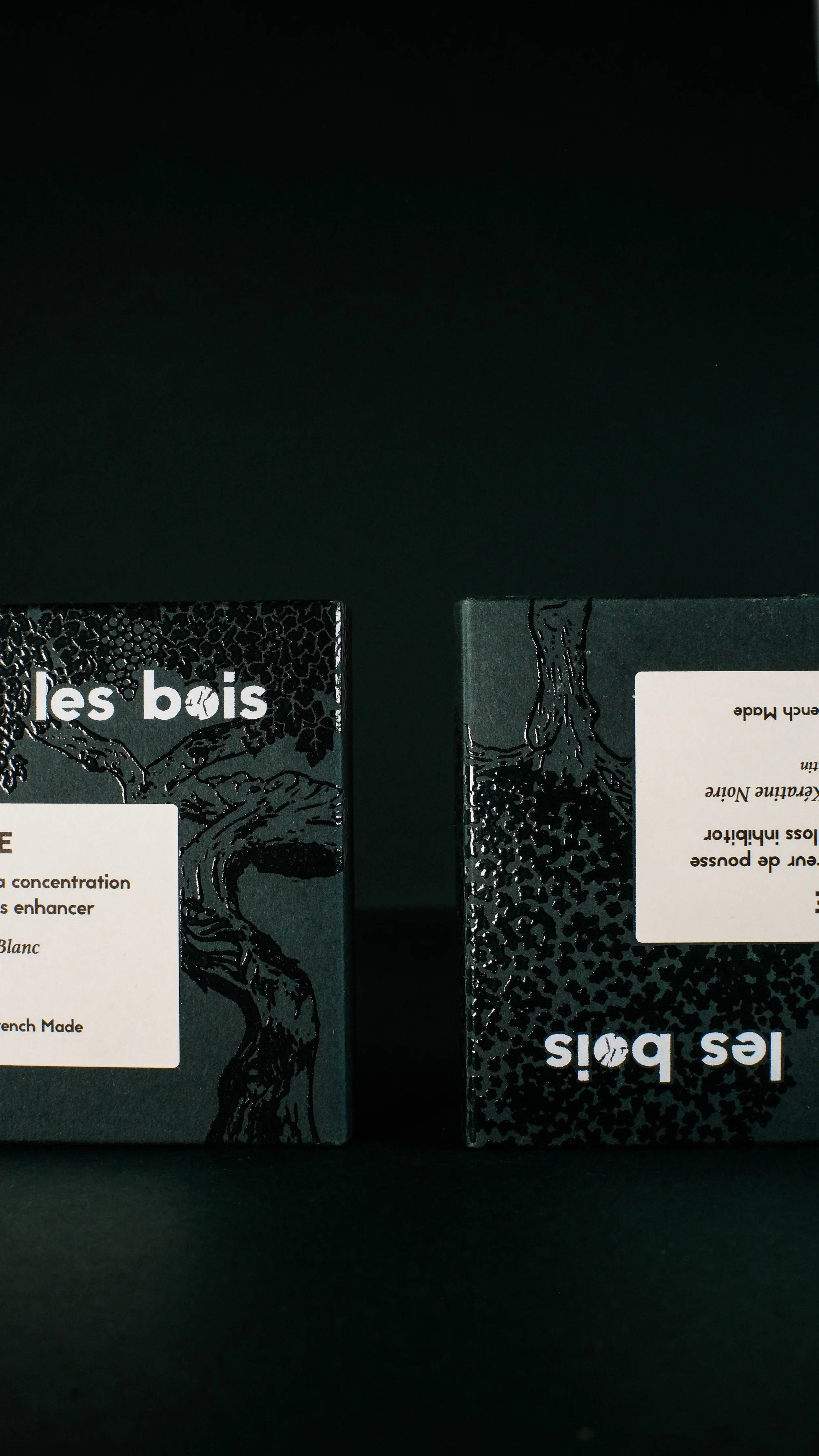 Deux boîtes de produits en forme de cubes, avec illustration d'un arbre stylisé et texte en français et anglais, sur un fond noir.