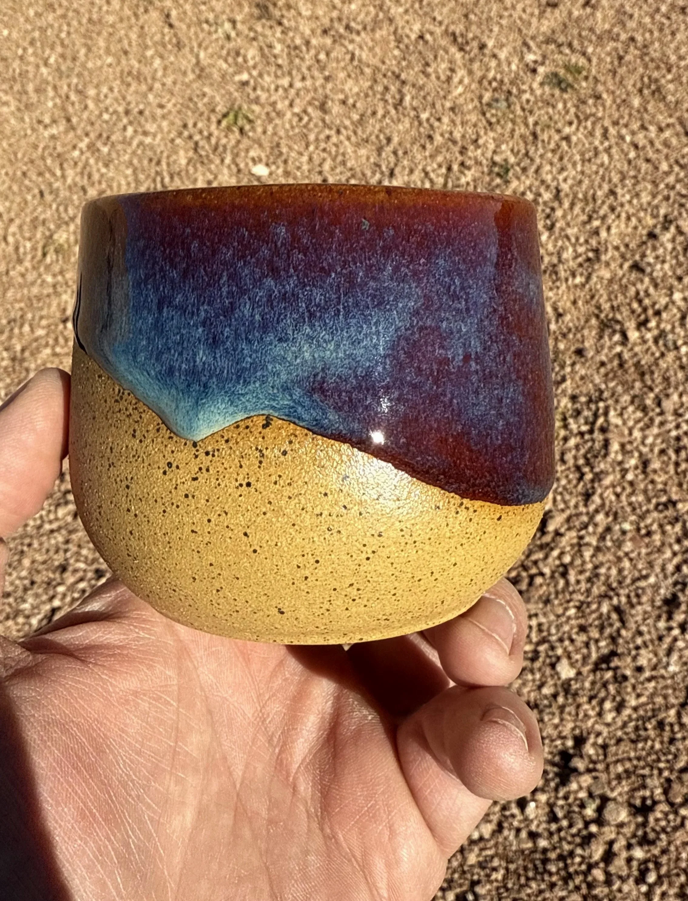 artist holding a desert sand tumbler with a drippy blue wine red glaze