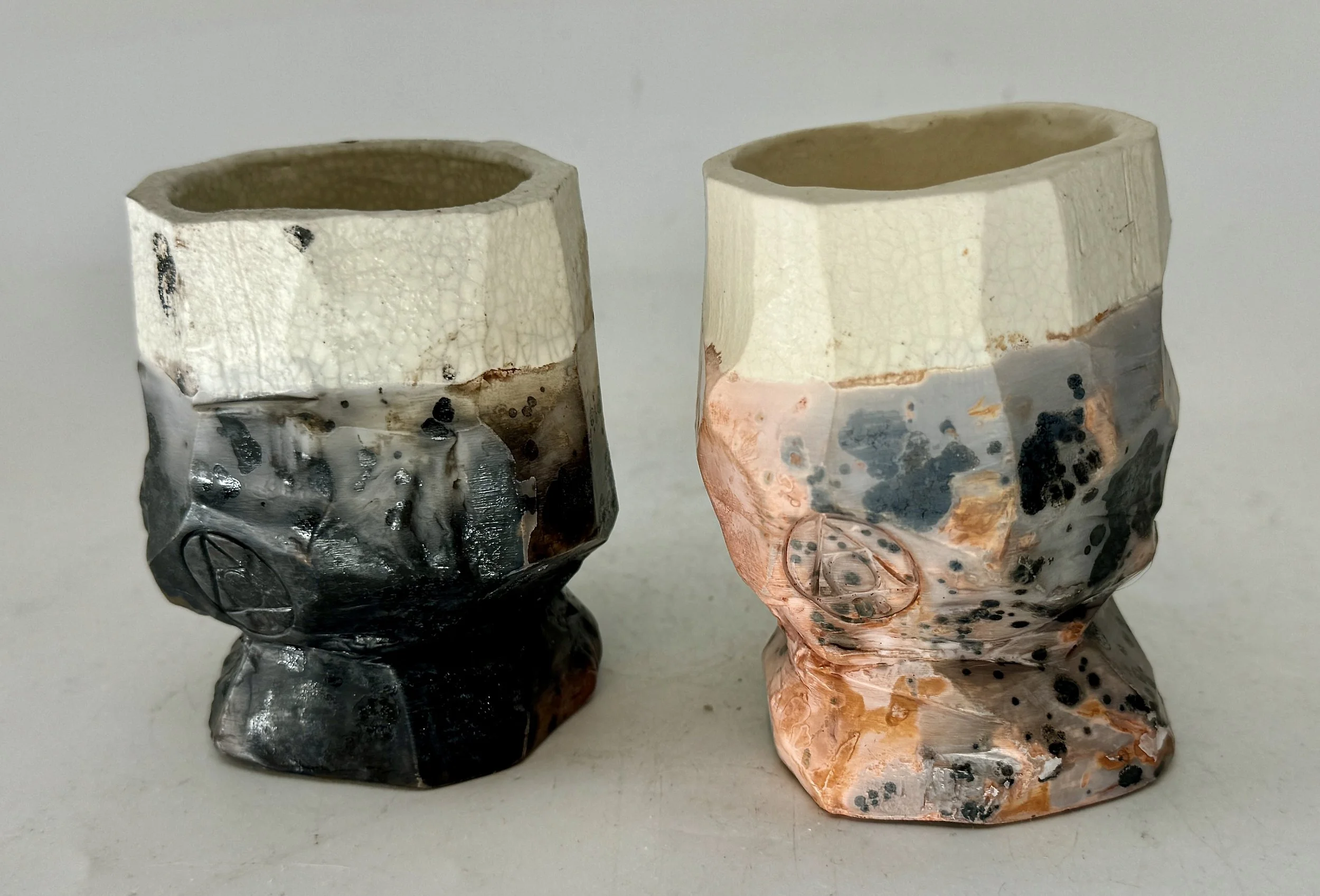 Two ceramic cups with geometric patterns in black, white, and orange, featuring textured, irregular surfaces with a glossy glaze finish.