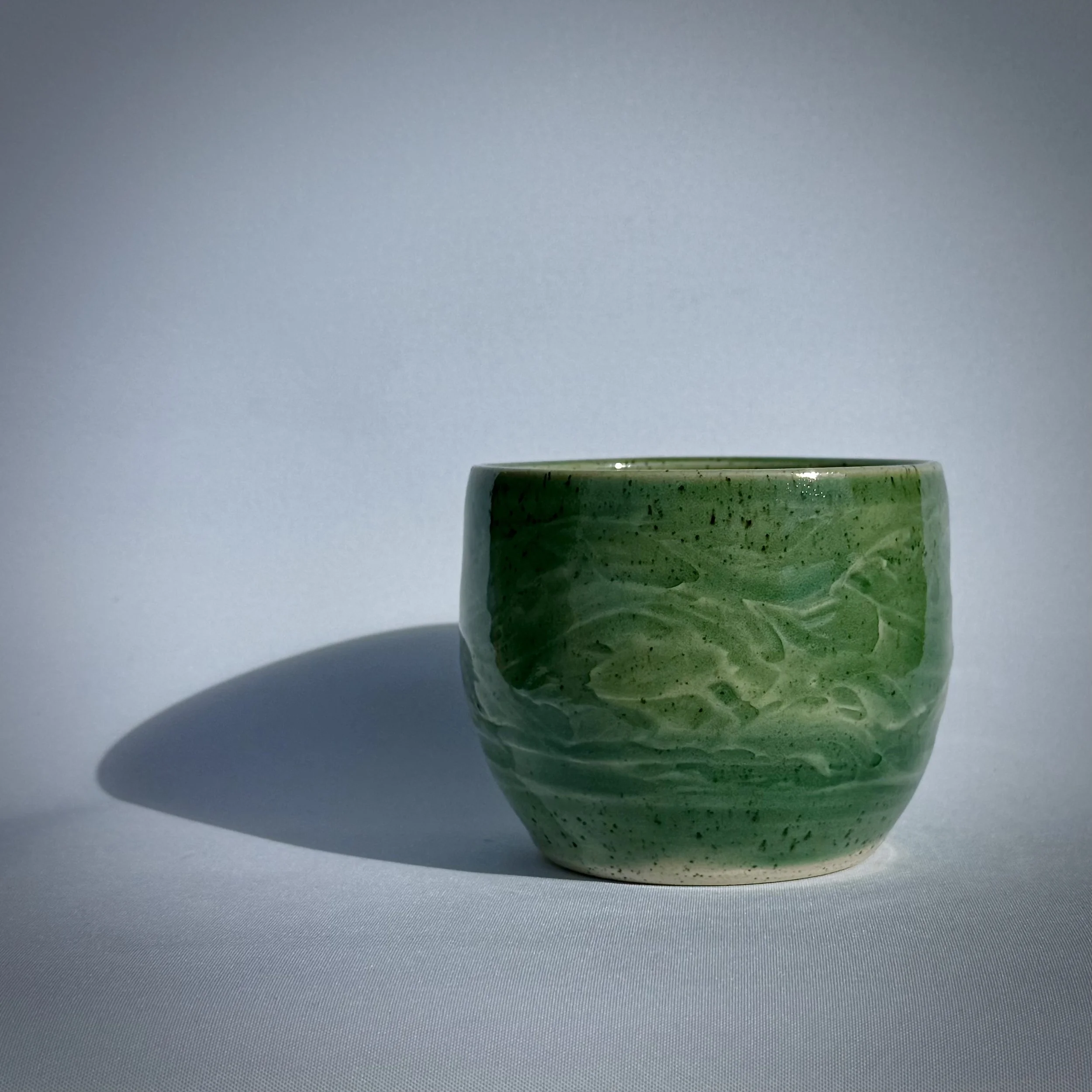 White tumbler with a flowing design glazed in green representing flowing water