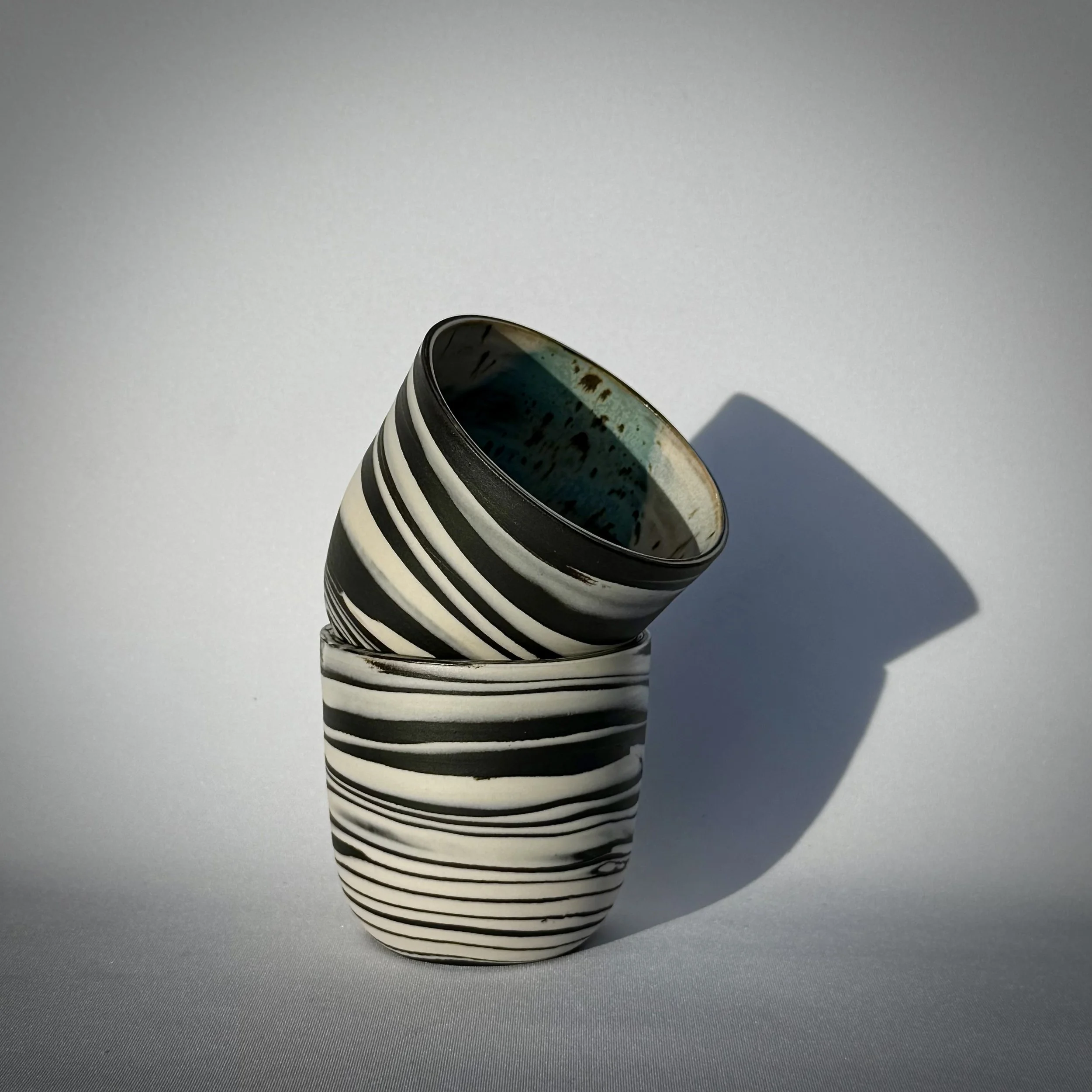 Two black and white striped swirled/marbled cups stacked, casting a shadow on a white surface under bright light