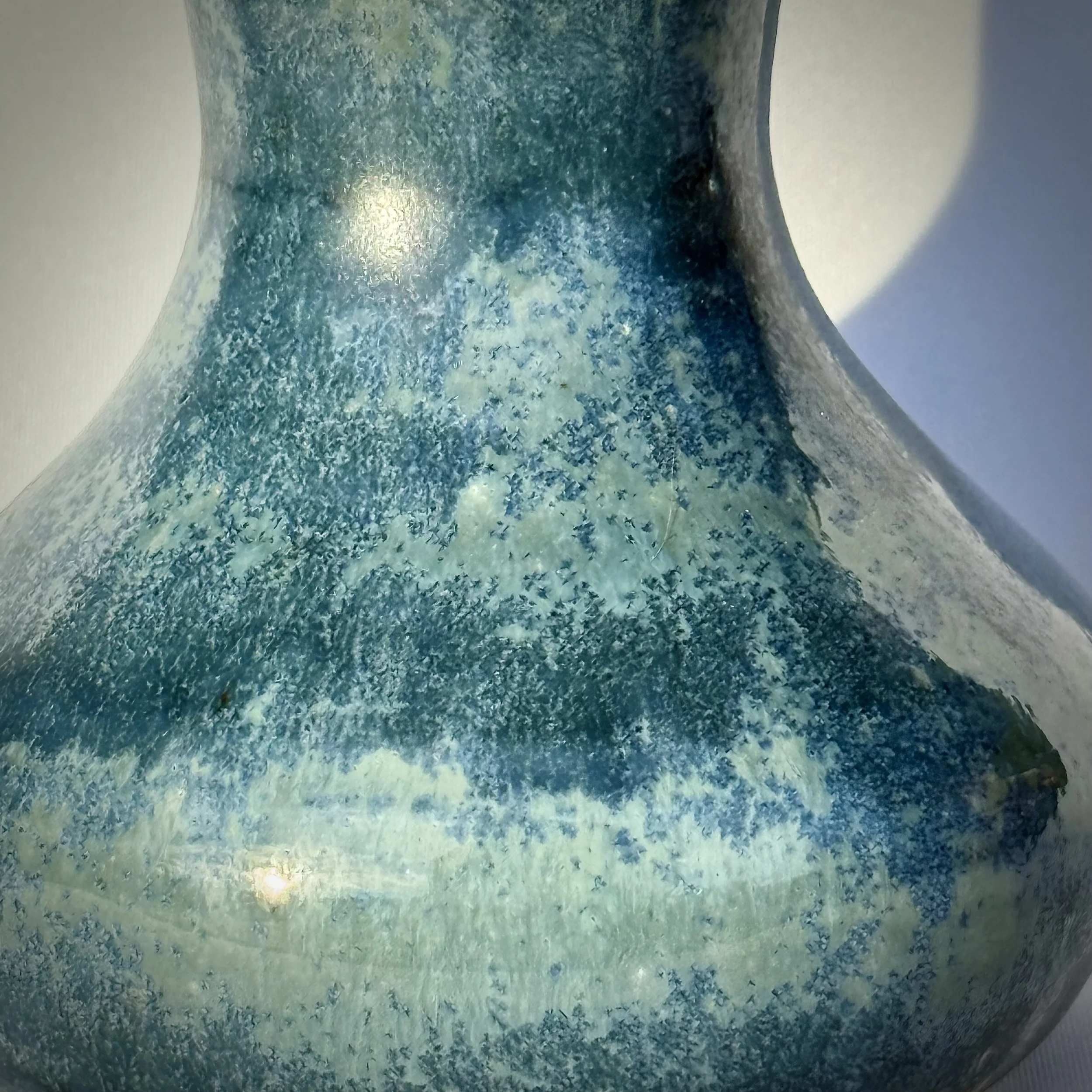 Close-up of a ceramic vase with a textured blue-green glaze that includes crystals.