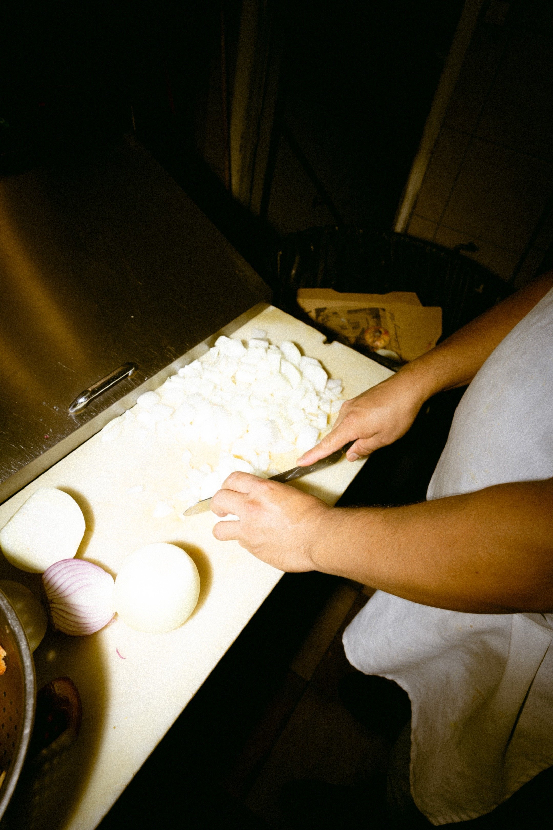 Person chopping white onions on a white cutting board in a kitchen.