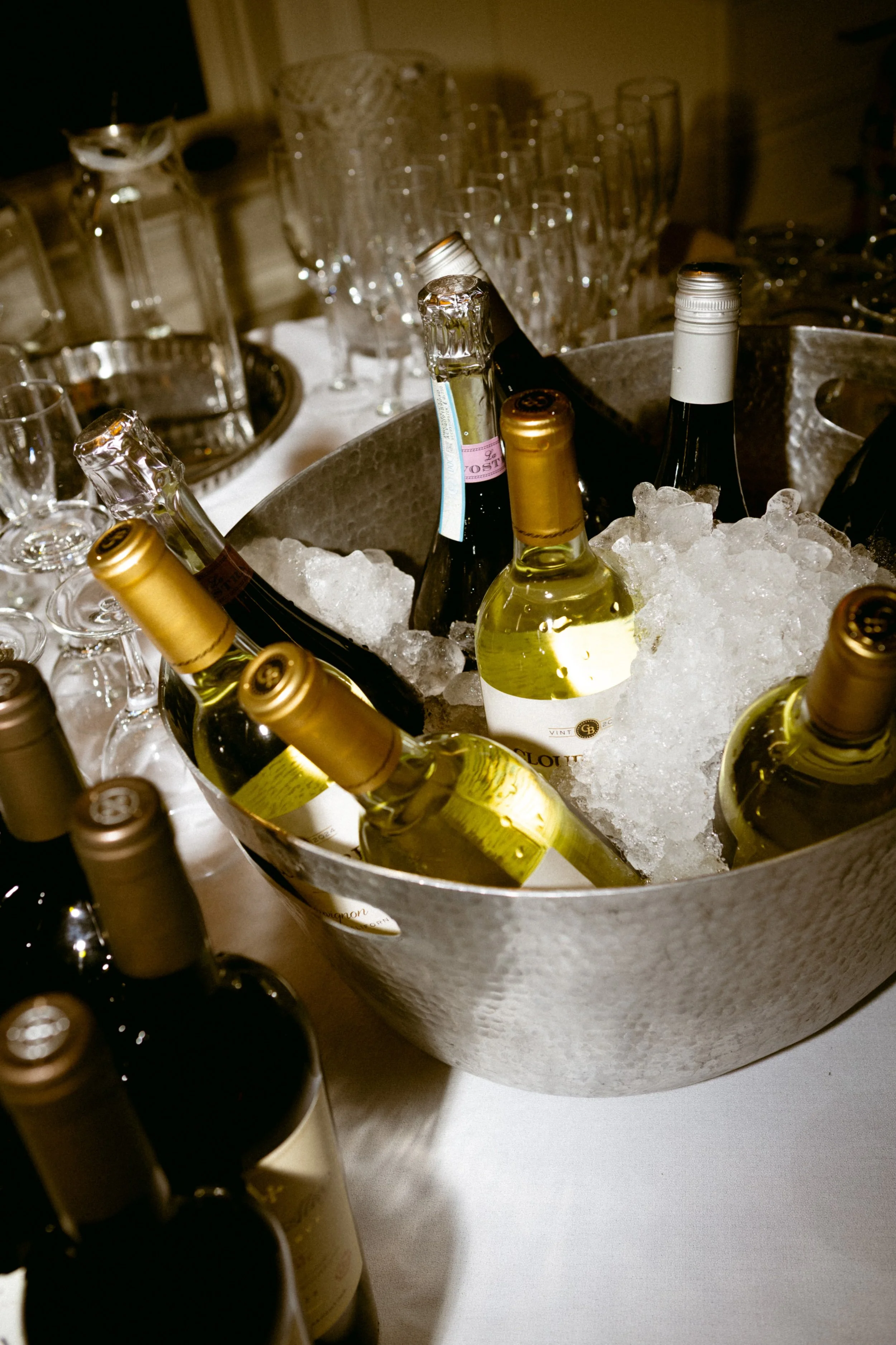 A metal ice bucket filled with ice and several bottles of white wine chilling inside.