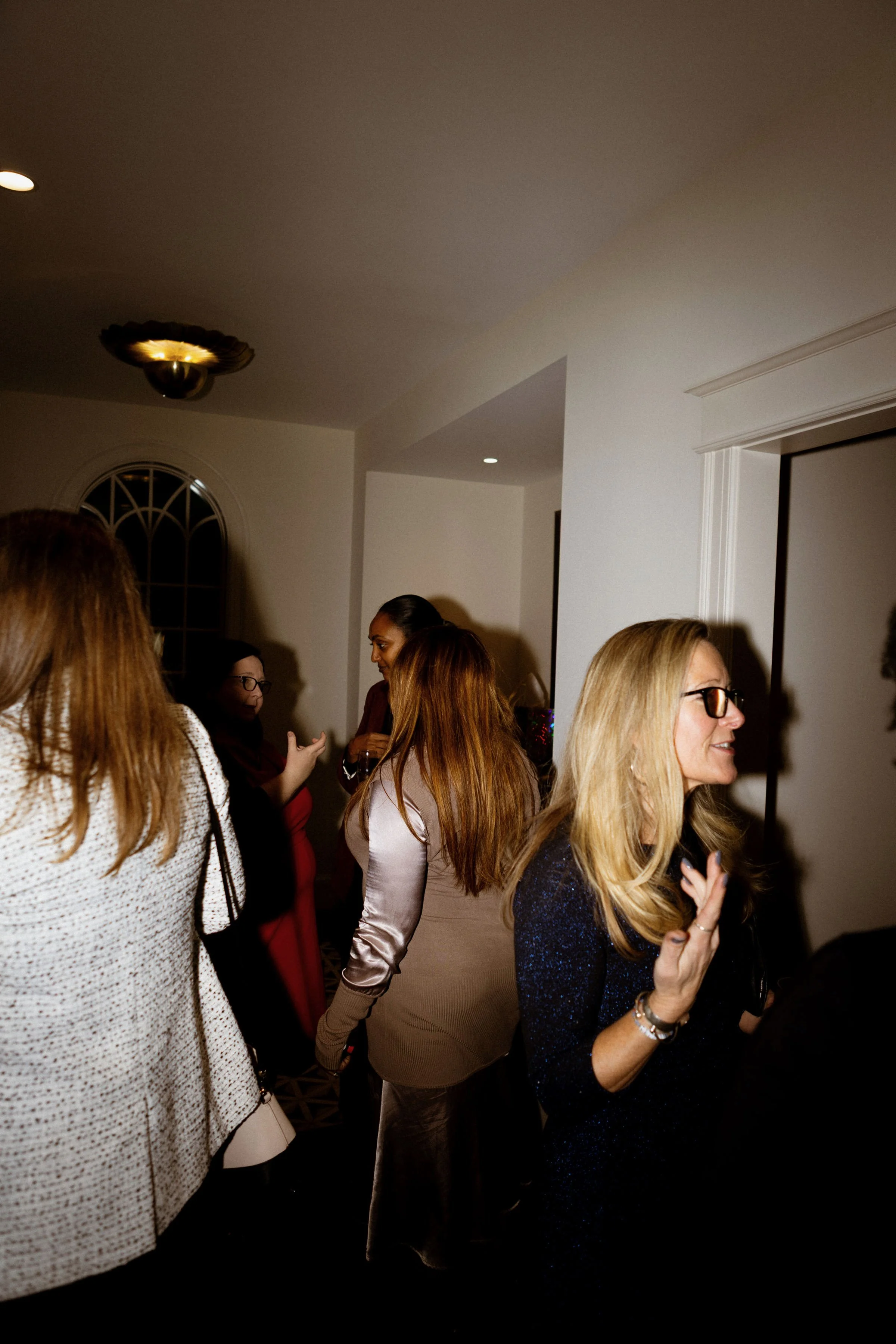 Group of women socializing indoors at a party, some smiling and engaging in conversation.