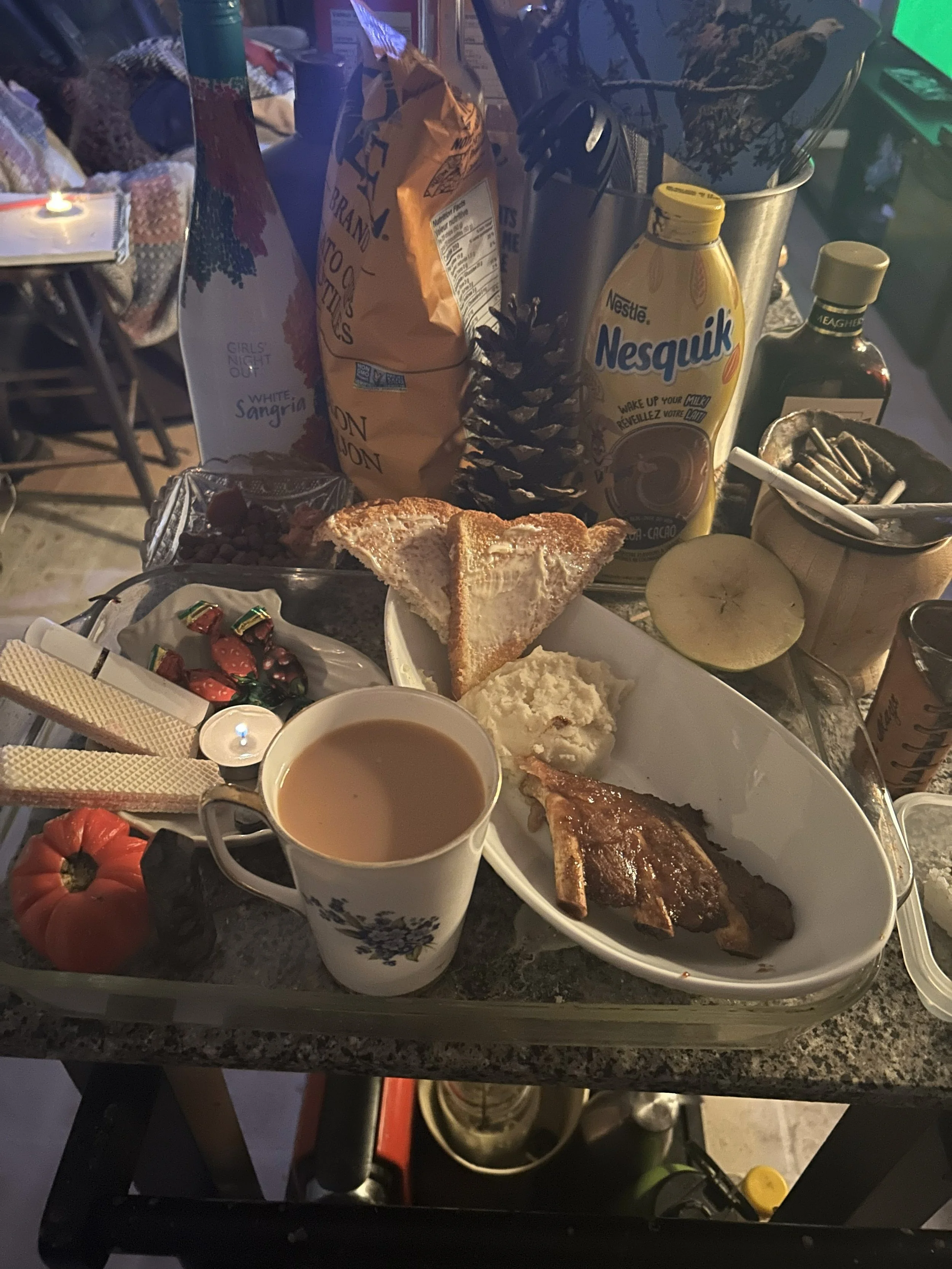 Breakfast tray with toast, mashed potatoes, sausage, and a cup of coffee, surrounded by condiments, snacks, and beverages on a kitchen counter.