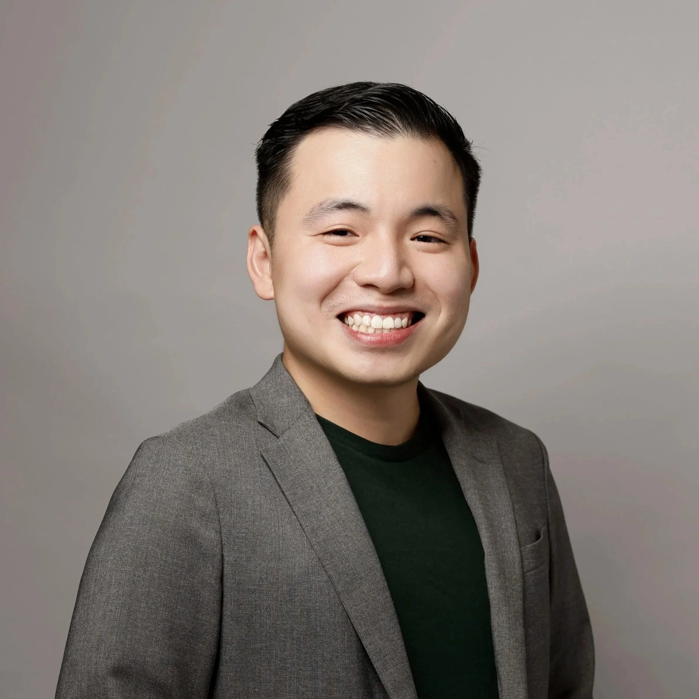 His name is Fong Mun Hong. Smiling young man with short black hair, wearing a gray blazer over a black shirt, against a neutral background.